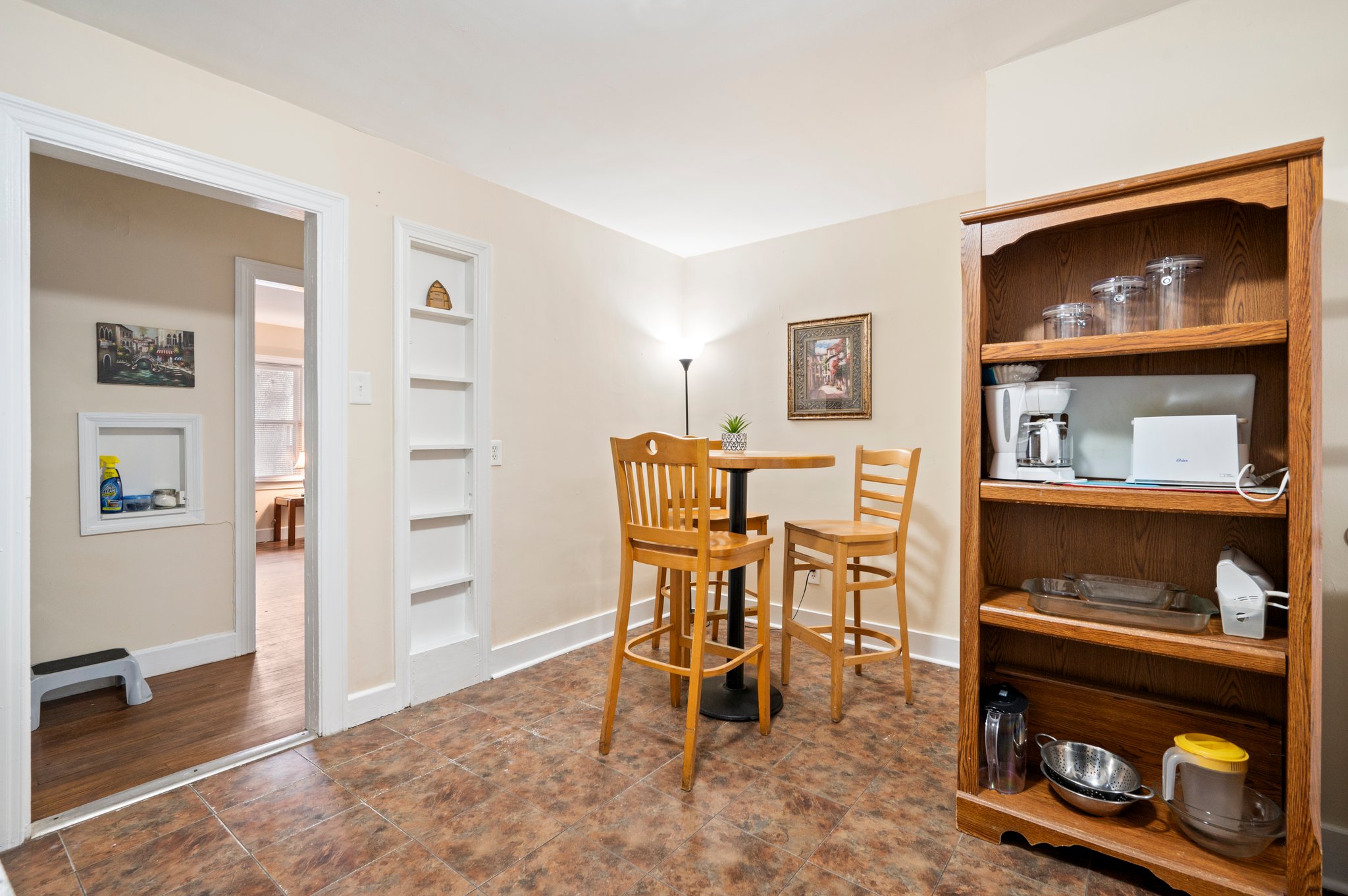 Dining area with wooden table and chairs, next to a wooden shelf with kitchenware.