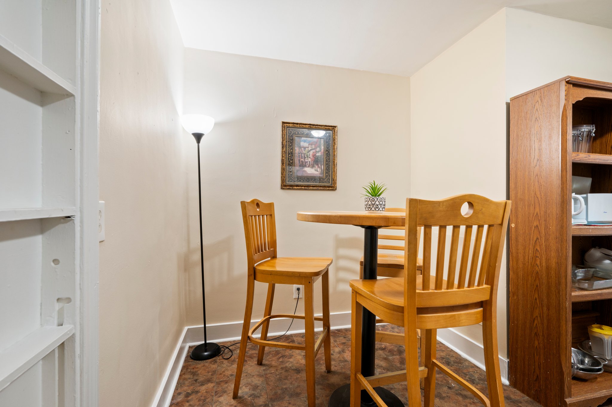 Small dining area with high-top wooden table and chairs, next to a bookshelf.