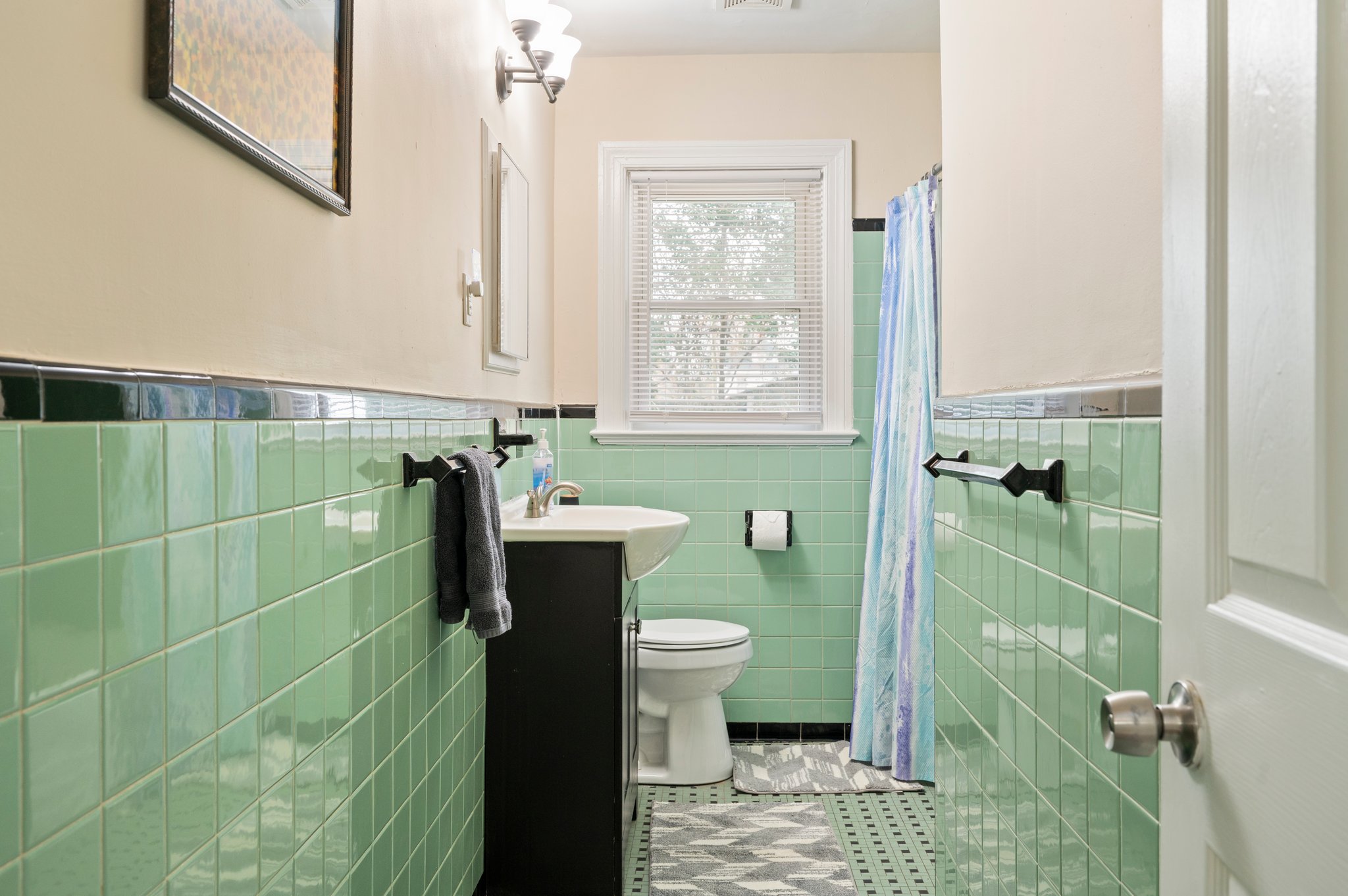 Bathroom with green tiled walls, white sink, and shower curtain.