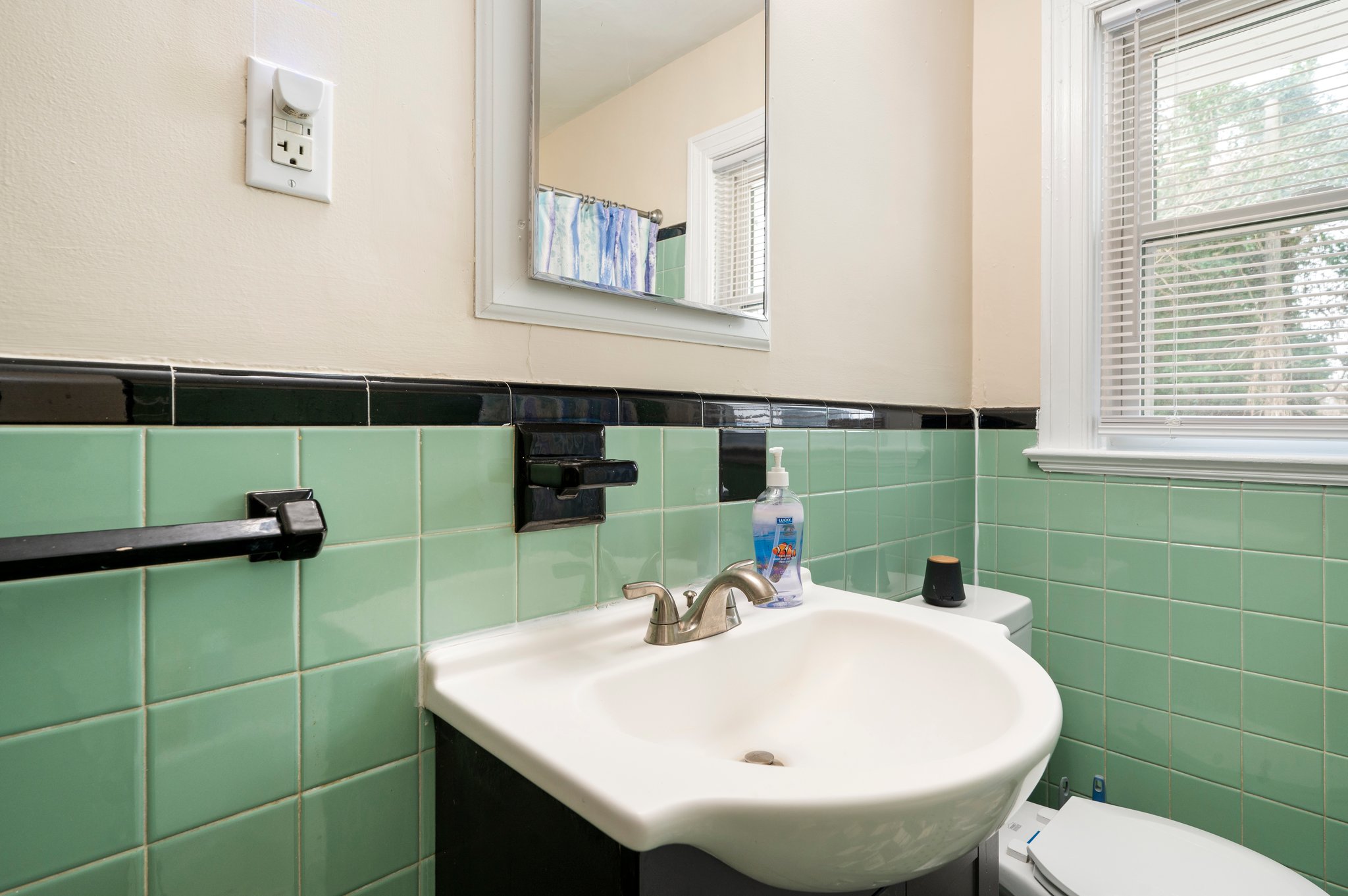 Close-up of a bathroom sink with a mirror and green tiled walls.