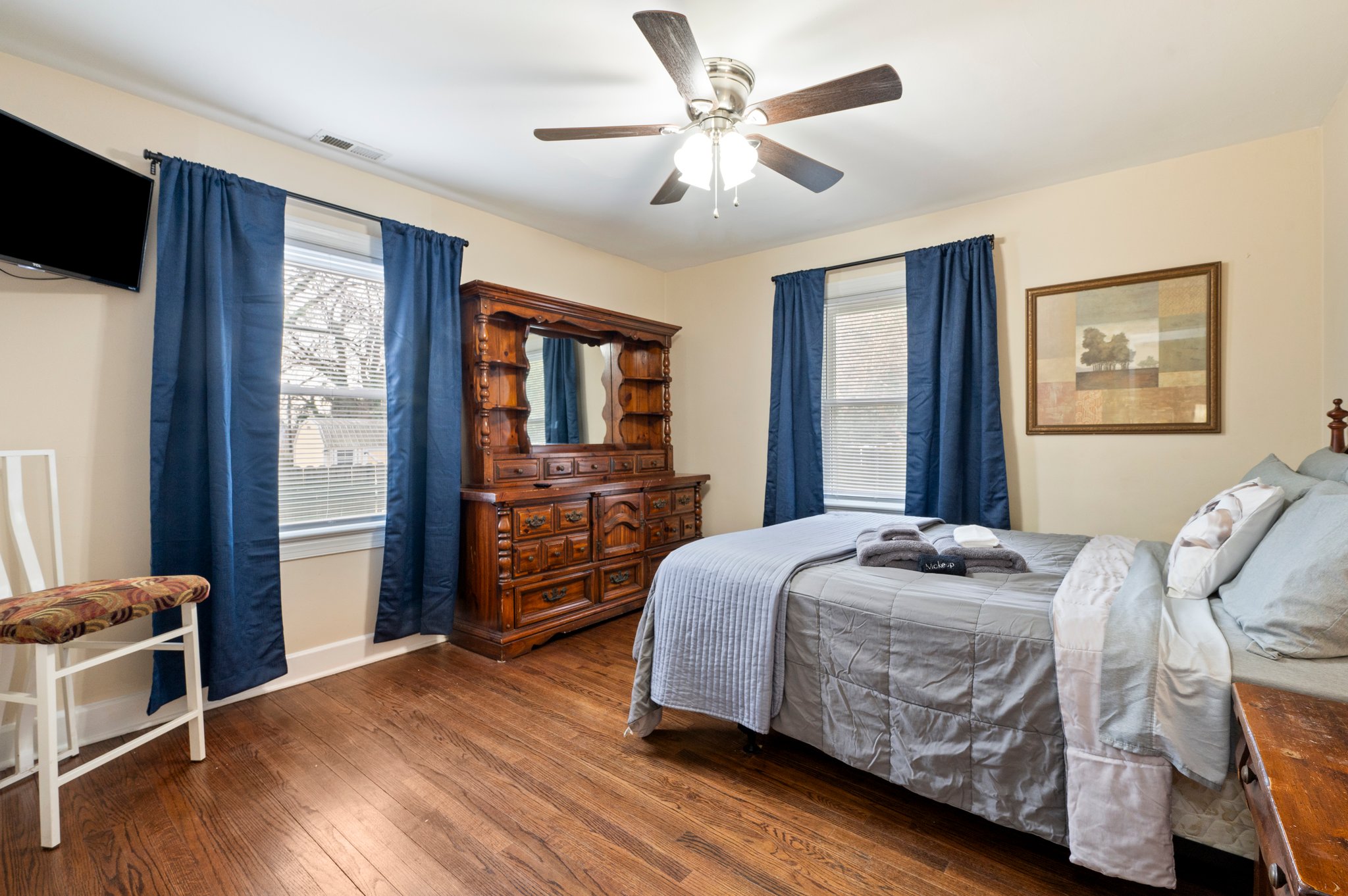 Bedroom with a large wooden dresser, blue curtains, and ceiling fan.