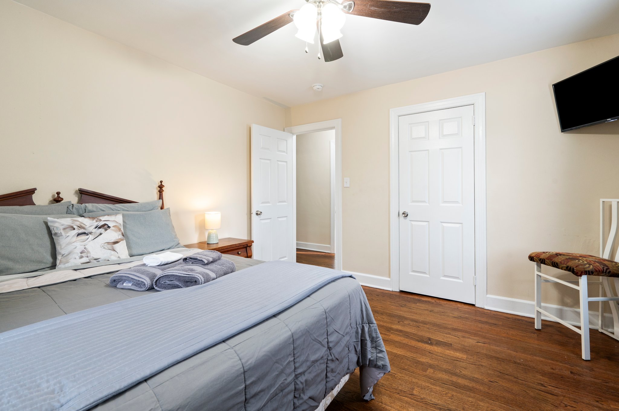 Bedroom with a neatly made bed, ceiling fan, and white closet doors.