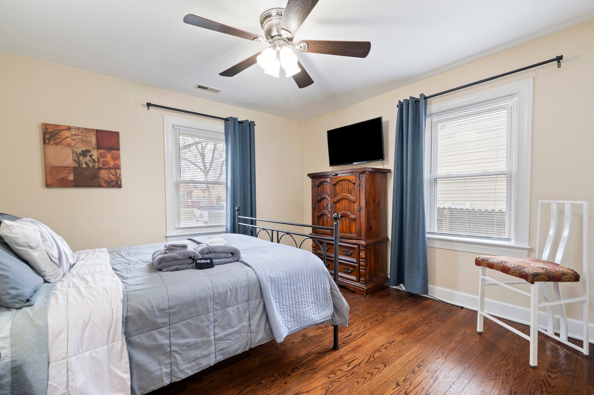 Bright bedroom with a metal frame bed, wooden furniture, and a TV.