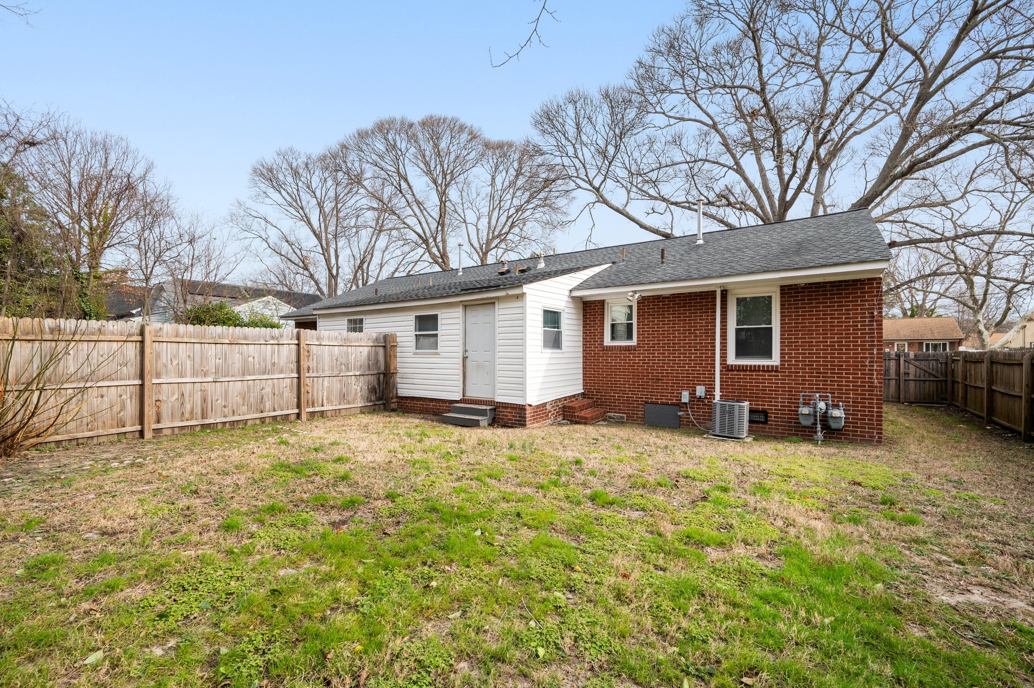 Fenced backyard with a red brick house and a small white storage area.