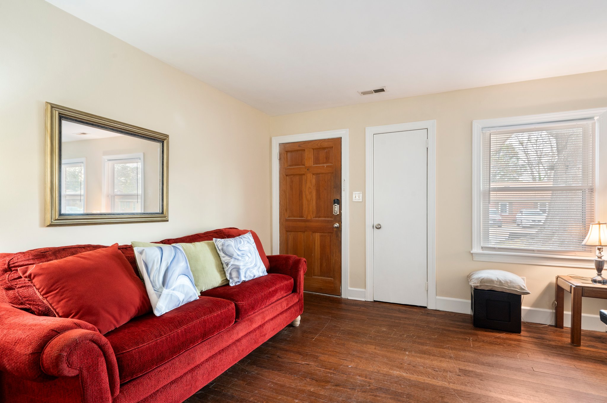 Living room with red sofa, wooden floors, and a mirror on the wall.