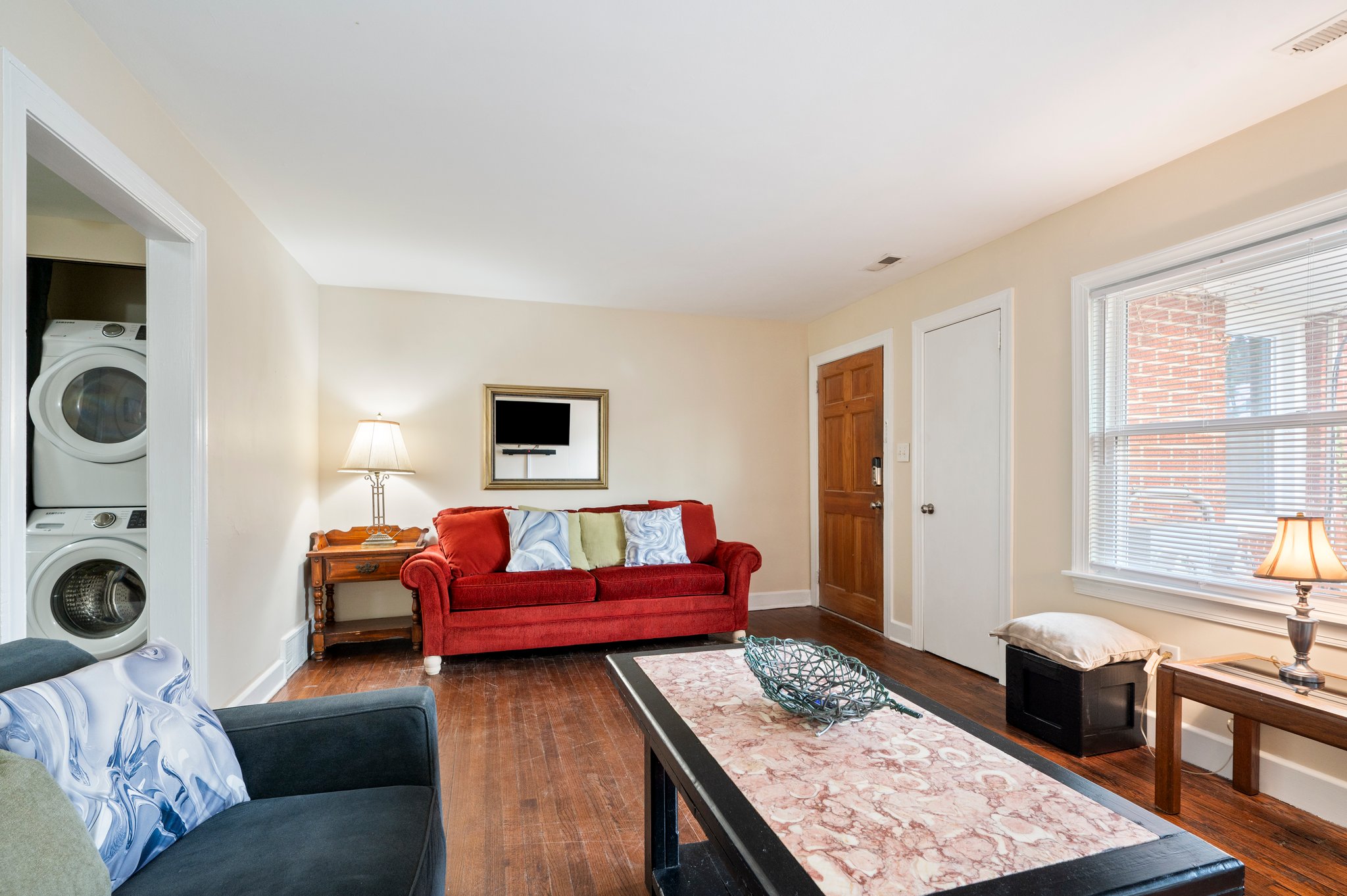 Living room with red sofa, wall-mounted TV, and stacked washer and dryer in view.