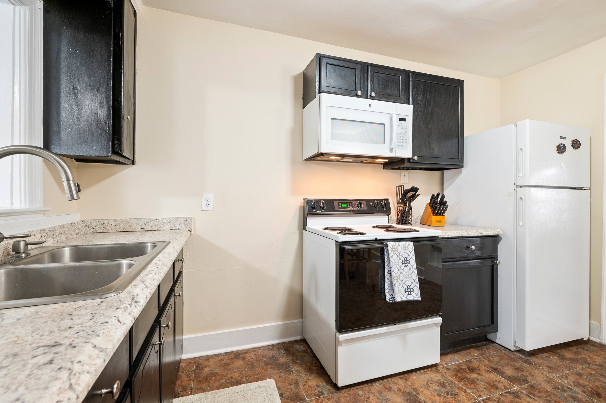 Close-up of a kitchen with a double sink, black cabinets, and a white stove.