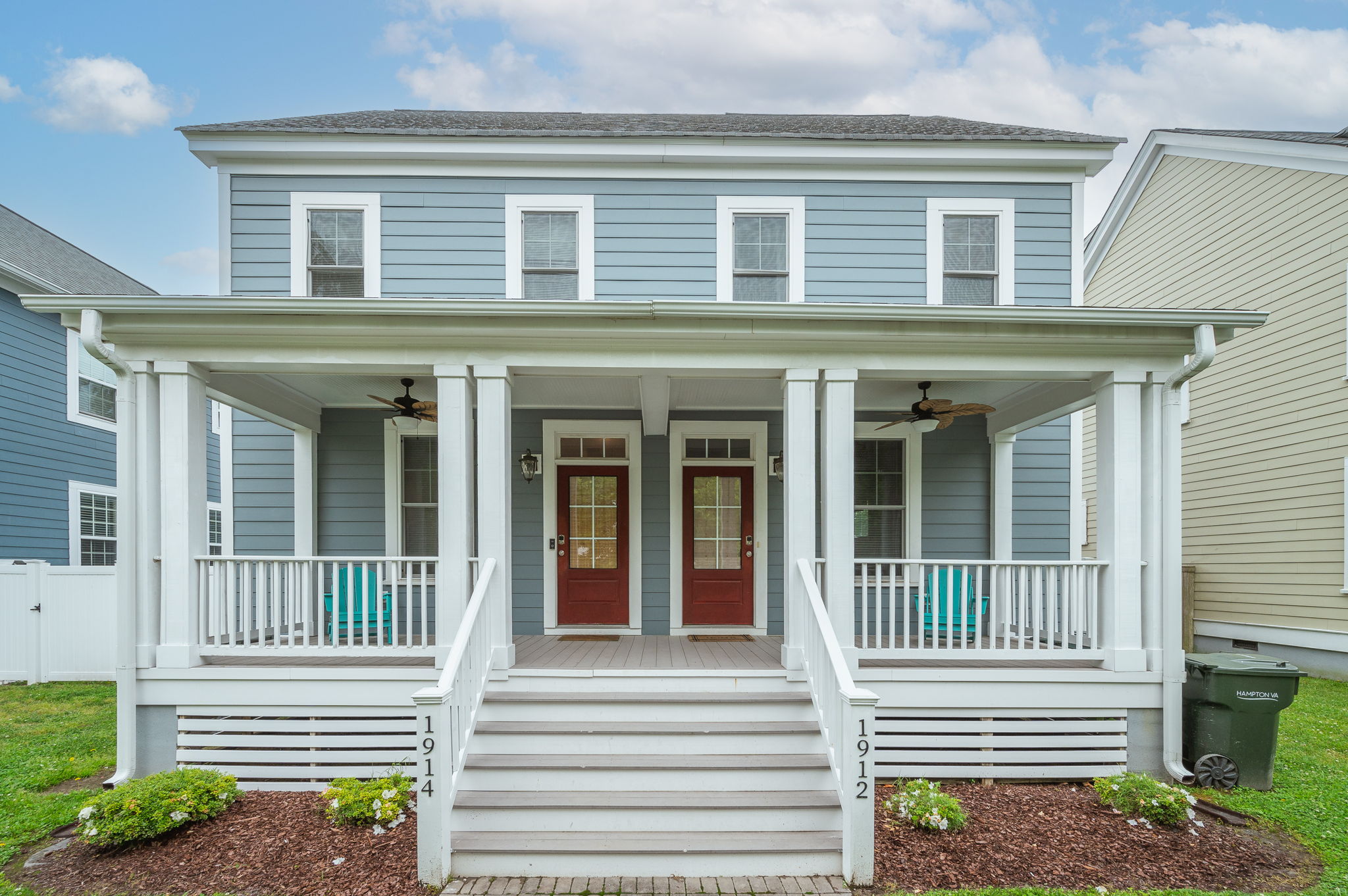 Front-facing view of a blue duplex with two red doors and a welcoming porch.