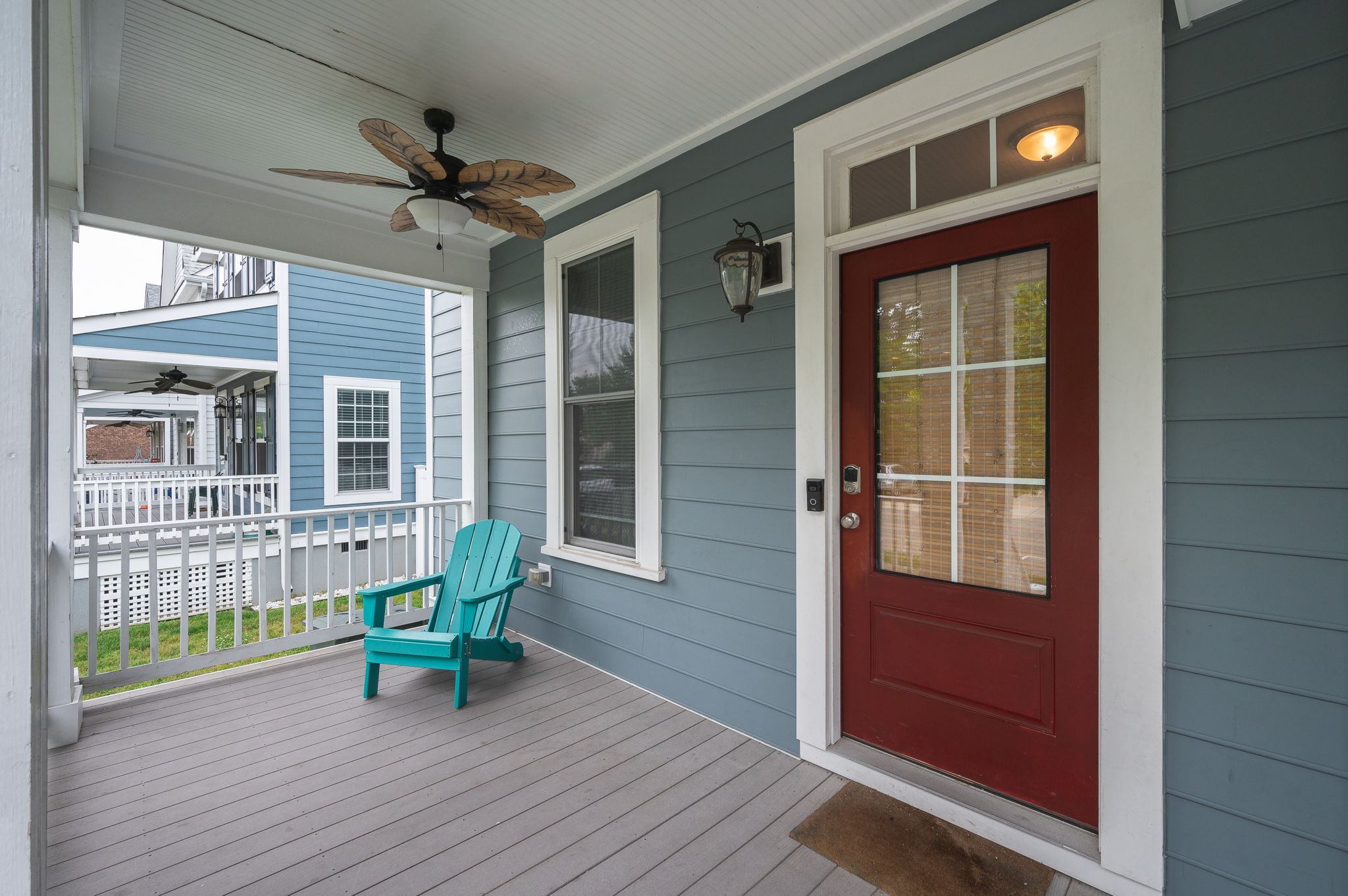 Close-up of the front porch of a blue duplex, featuring a red door and a turquoise Adirondack chair.