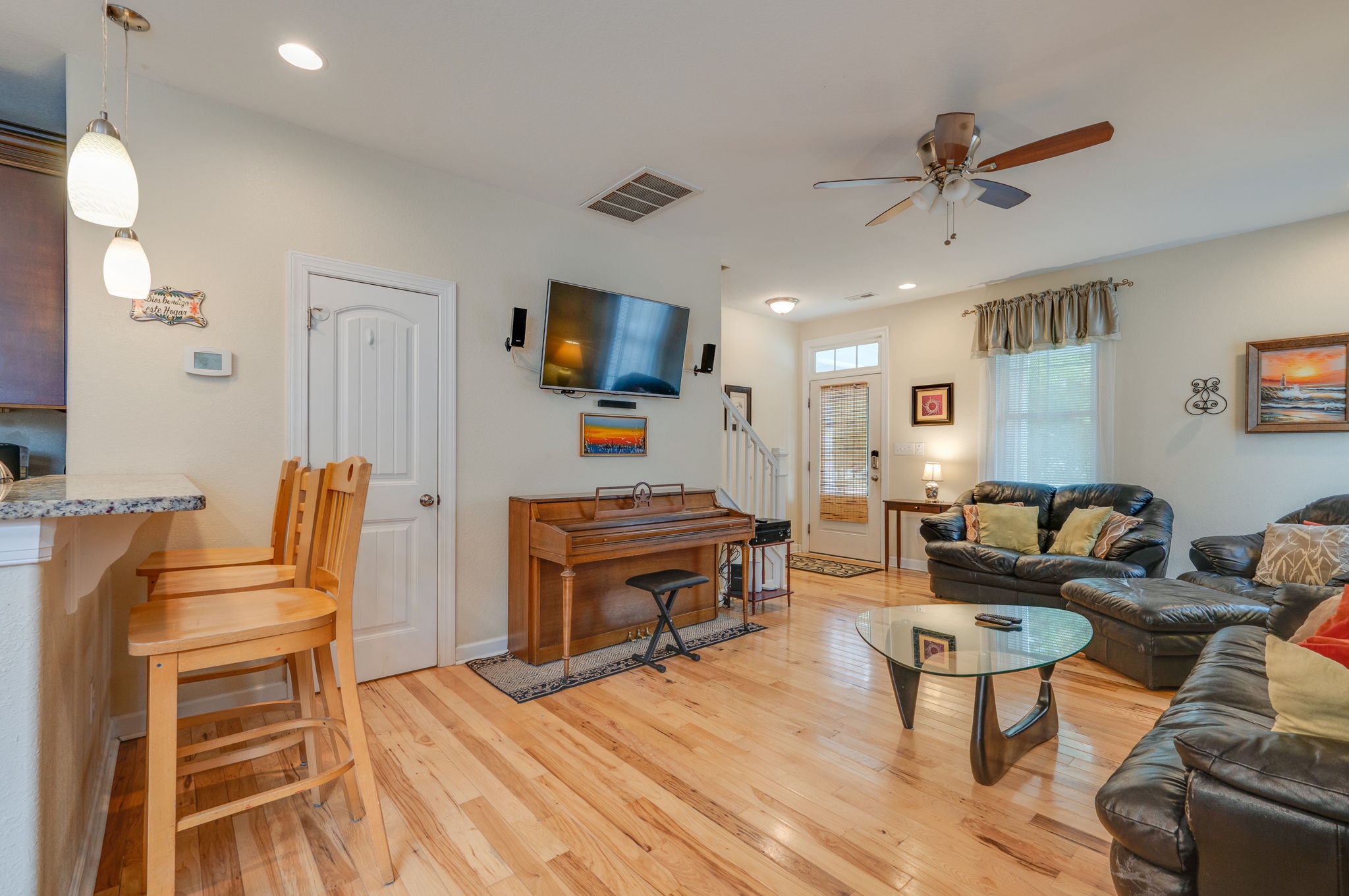 View of the living room with a mounted TV, wooden piano, and an open-concept design.