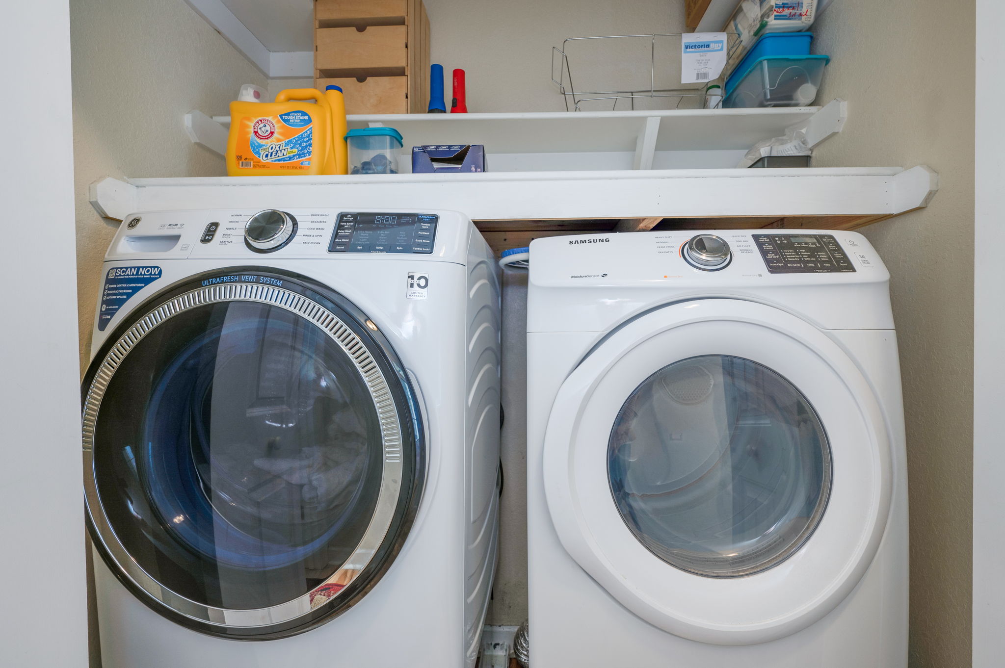 Laundry area with modern front-loading washer and dryer, storage shelves above.