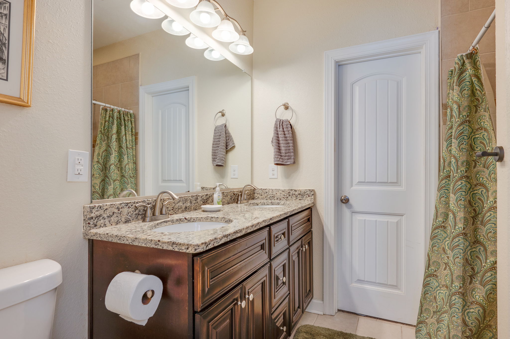 Modern bathroom with double vanity, granite countertops, and decorative accents.