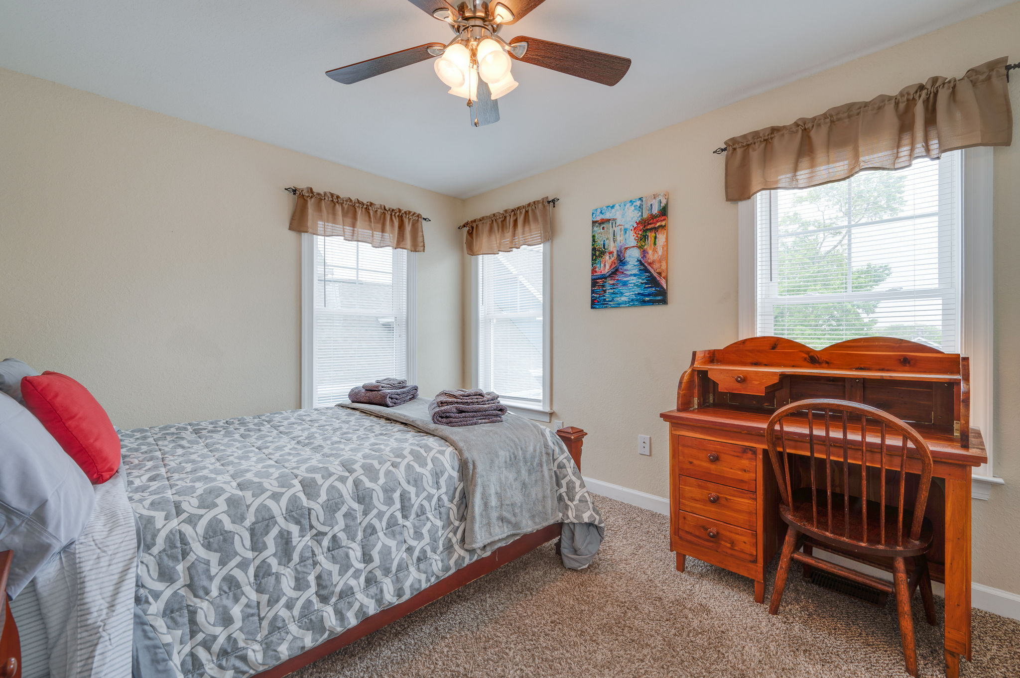 Bright bedroom with a single bed, a wooden desk, and large windows.