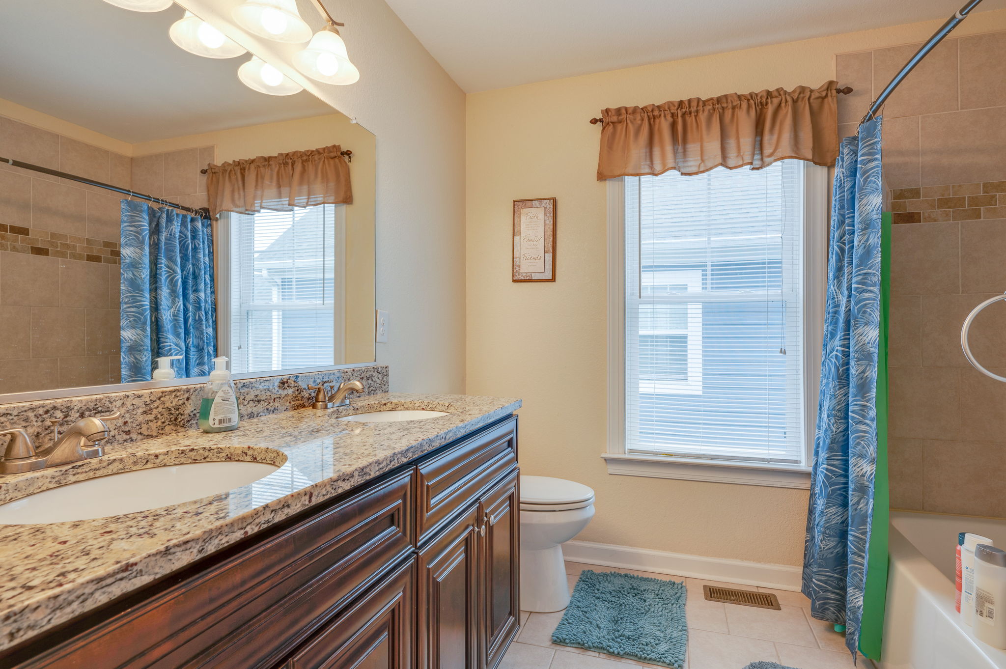Stylish bathroom with a dual sink, granite countertops, and a bathtub with a blue curtain.