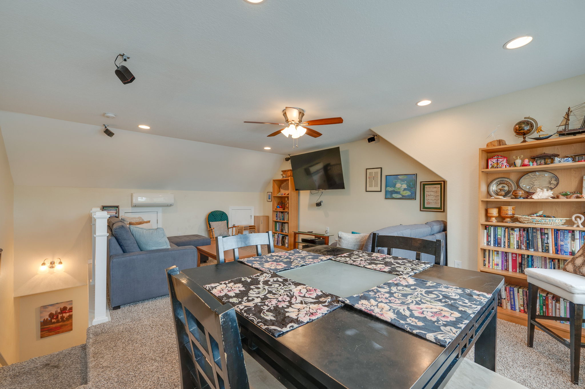 Upstairs loft area with a seating space, TV, bookshelves, and a dining table.
