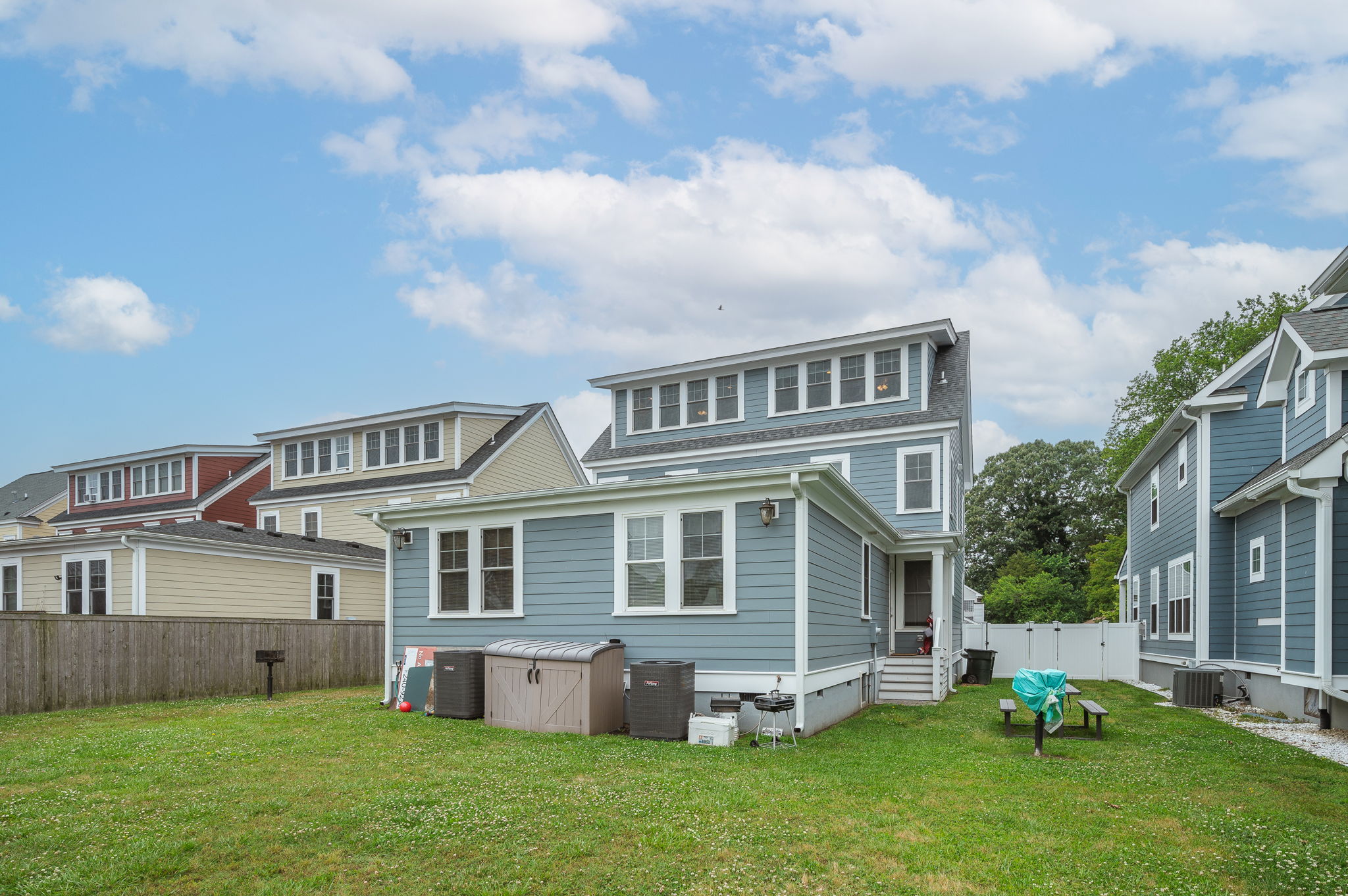 Backyard view of a blue multi-story home with green grass and a picnic area.