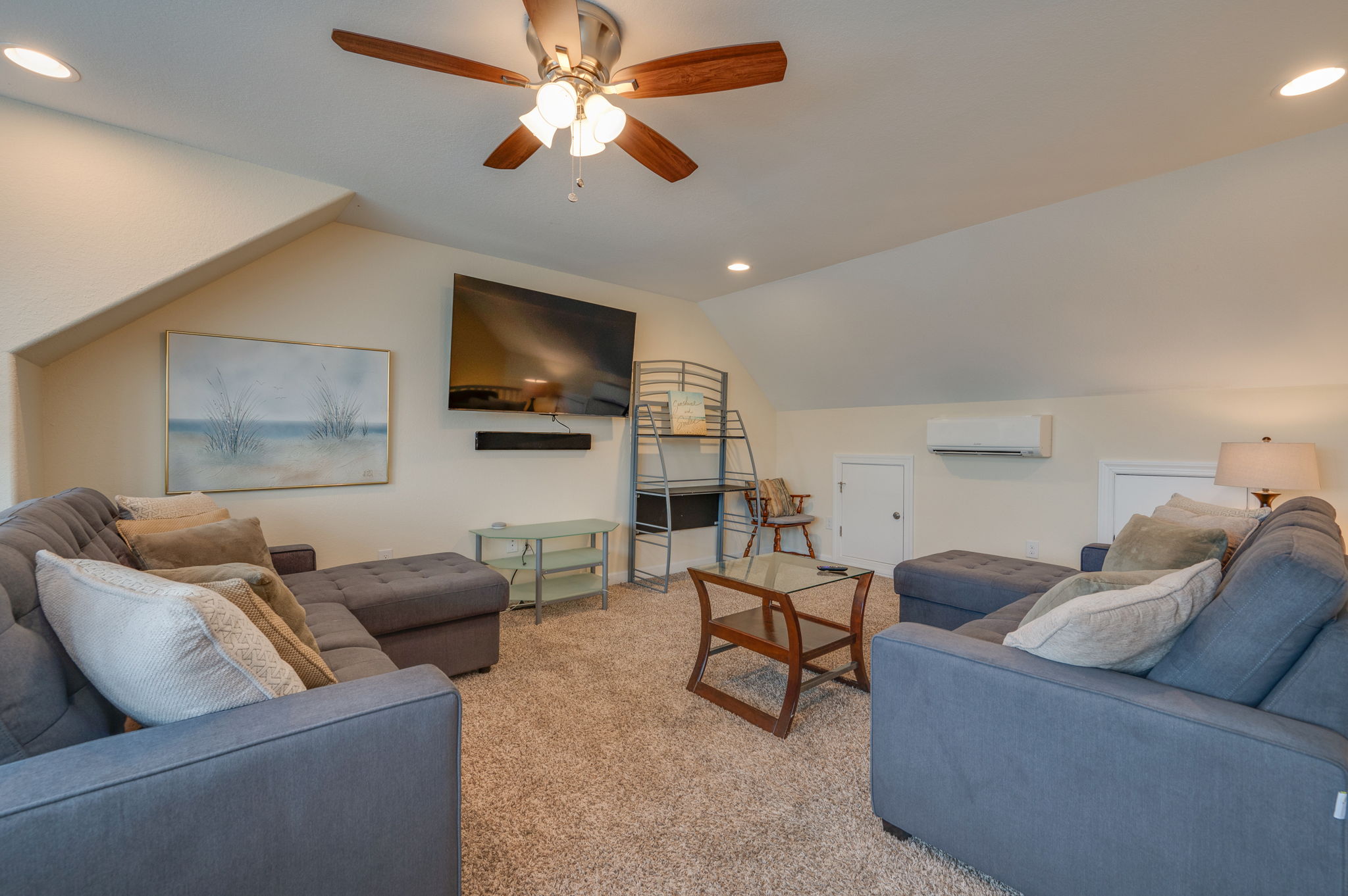 Spacious upstairs loft with a large sectional sofa, mounted TV, and soft lighting.