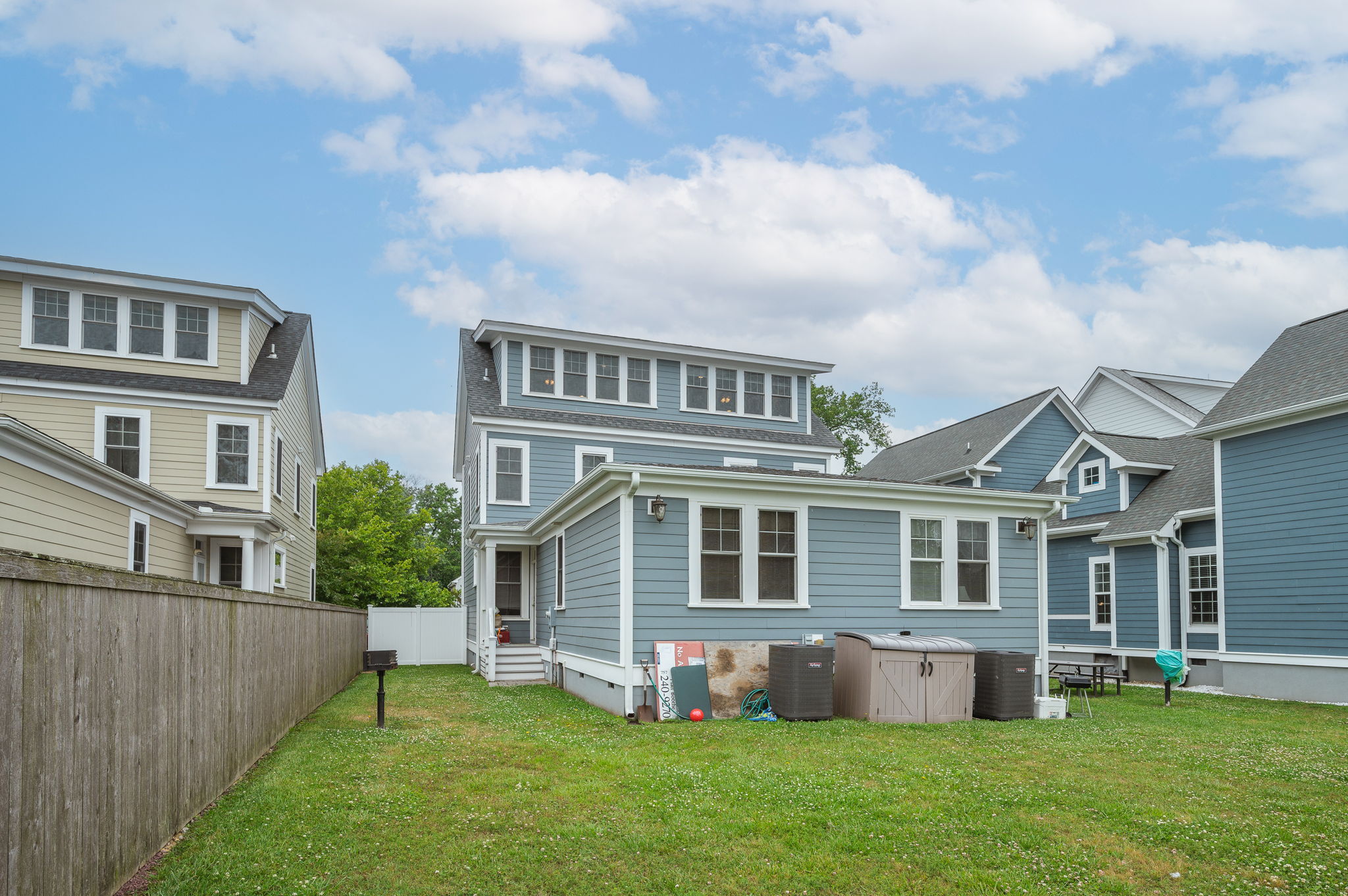 Backyard view of a blue three-story home with a well-maintained lawn and storage area.