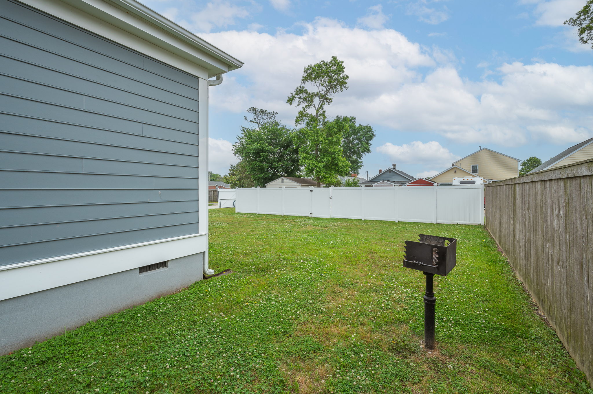 Side yard with a built-in grill and fenced-in green space for outdoor activities.