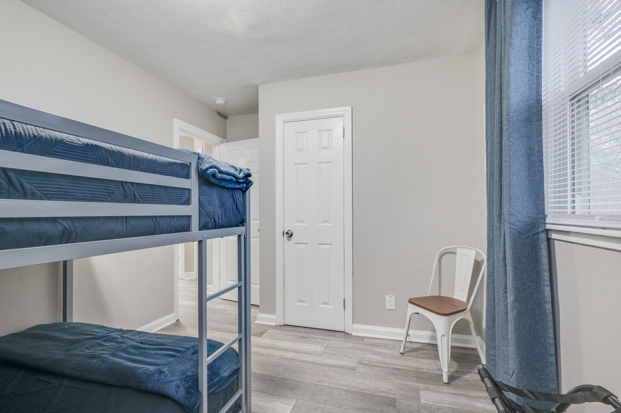 Minimalist bedroom with a bunk bed, white chair, and blue curtains.