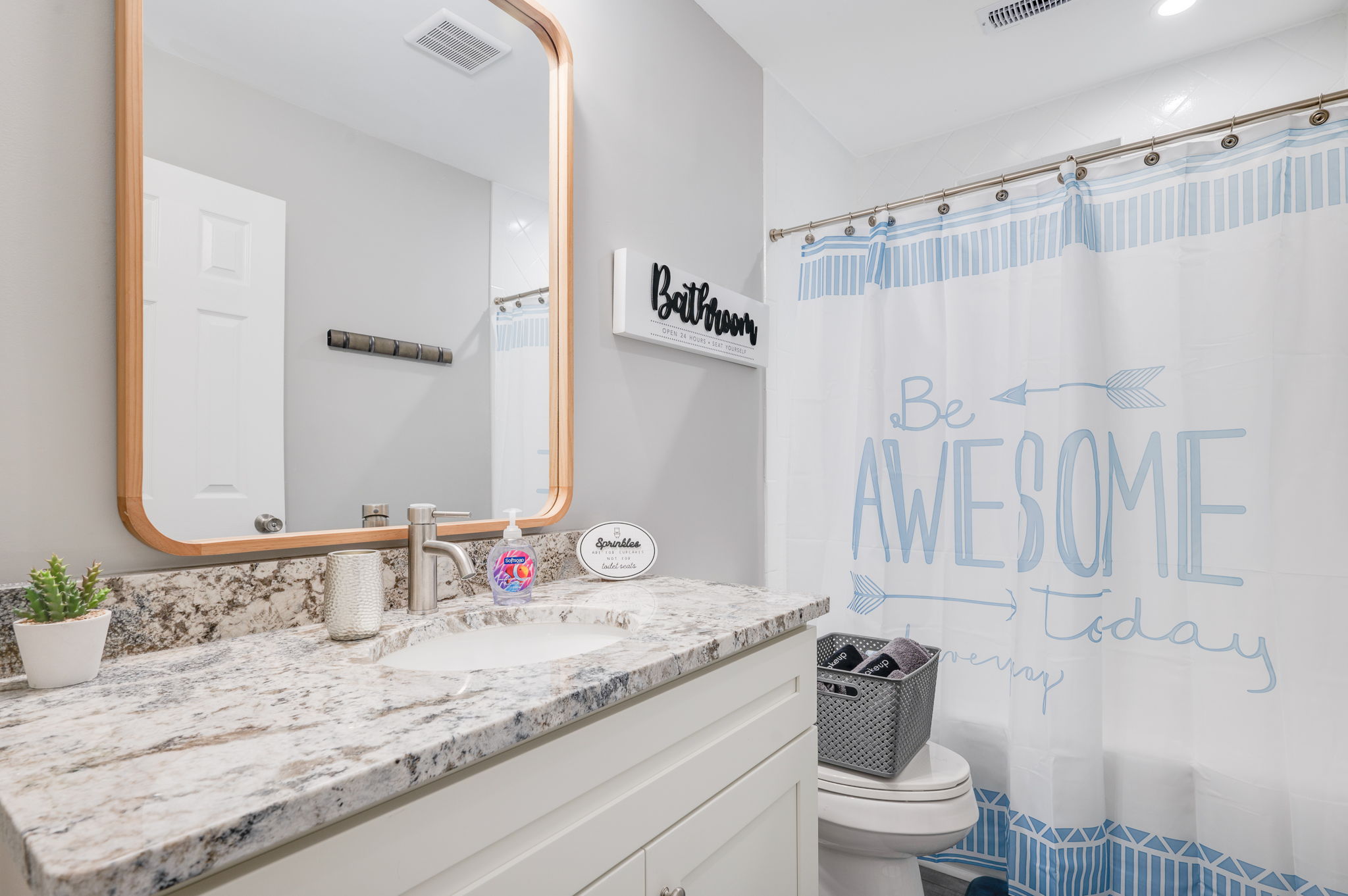 Modern bathroom with a granite countertop, large mirror, and motivational decor.