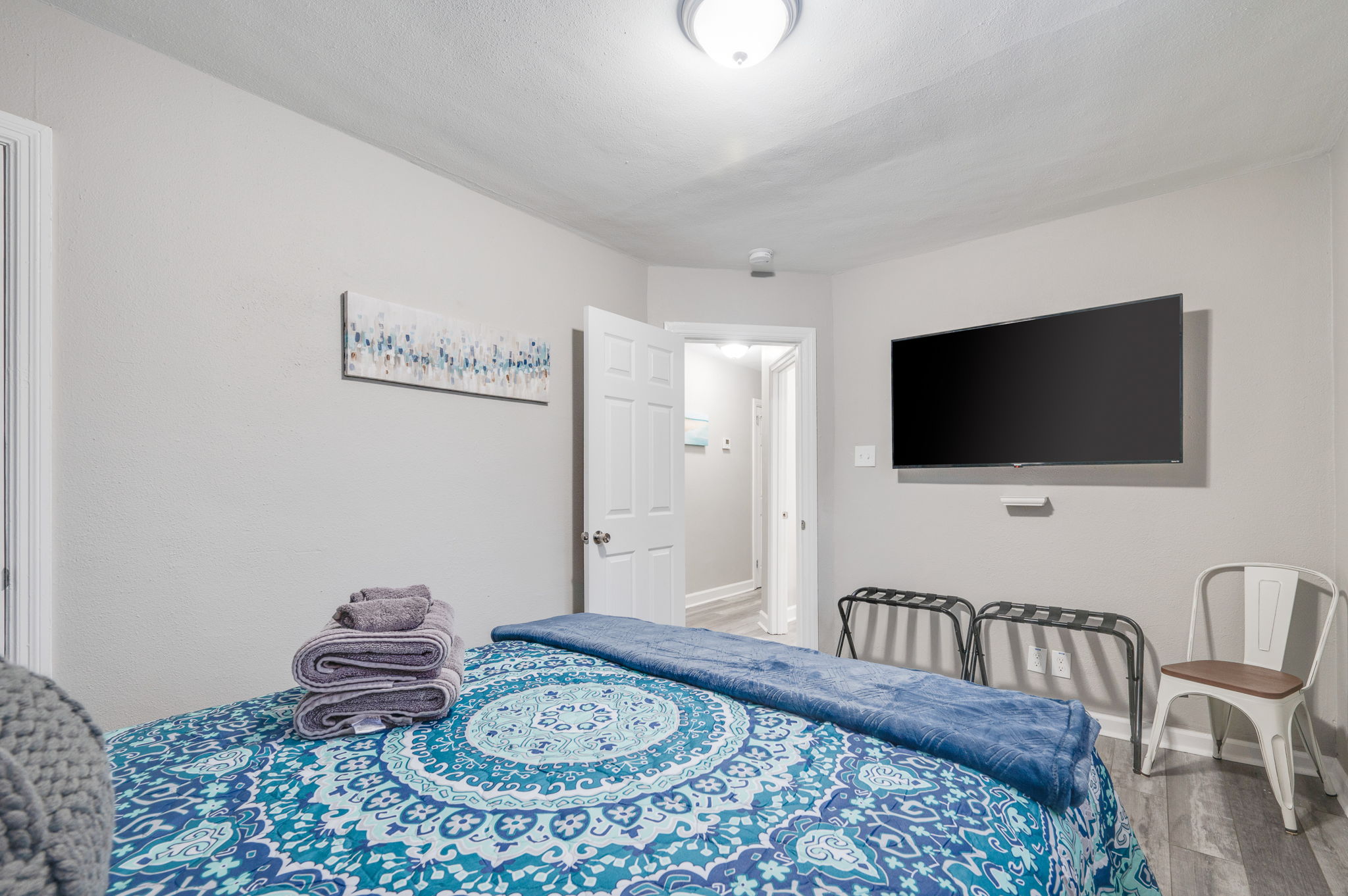 Cozy bedroom with blue and patterned bedding, a mounted TV, and simple decor.