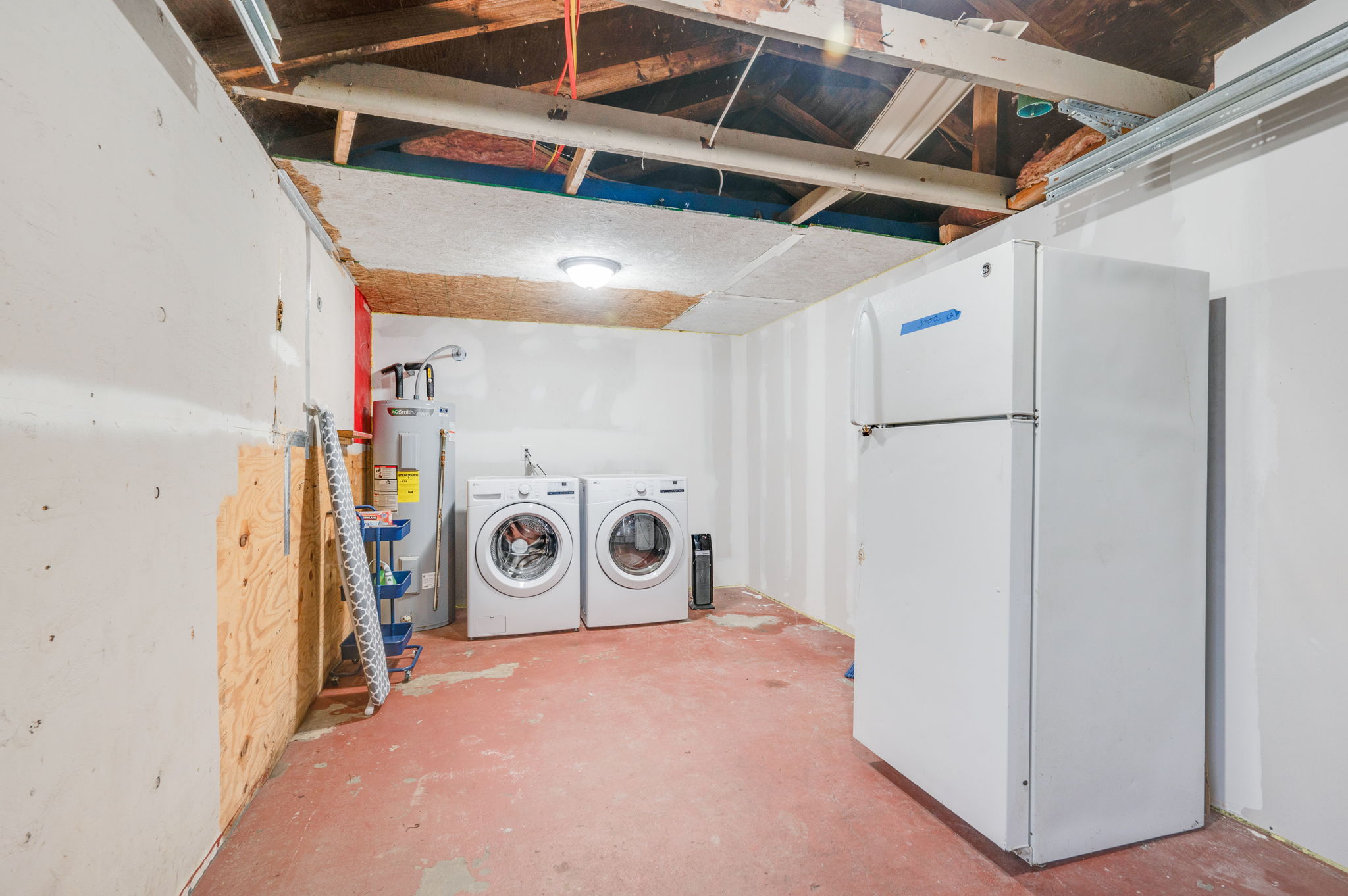 Laundry room with a washer, dryer, refrigerator, and exposed ceiling.