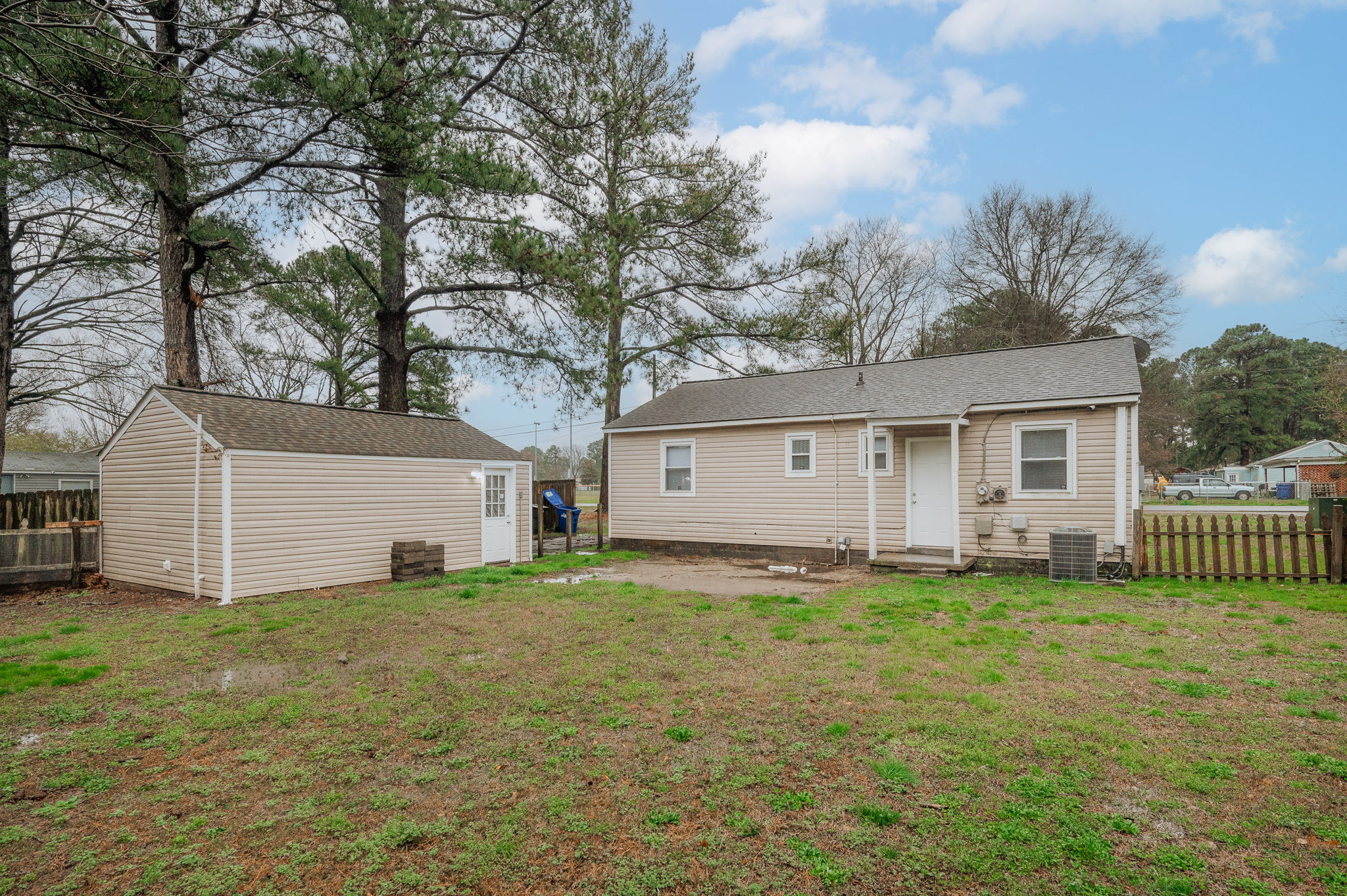 Backyard view of the home with a storage shed, grass, and surrounding trees.