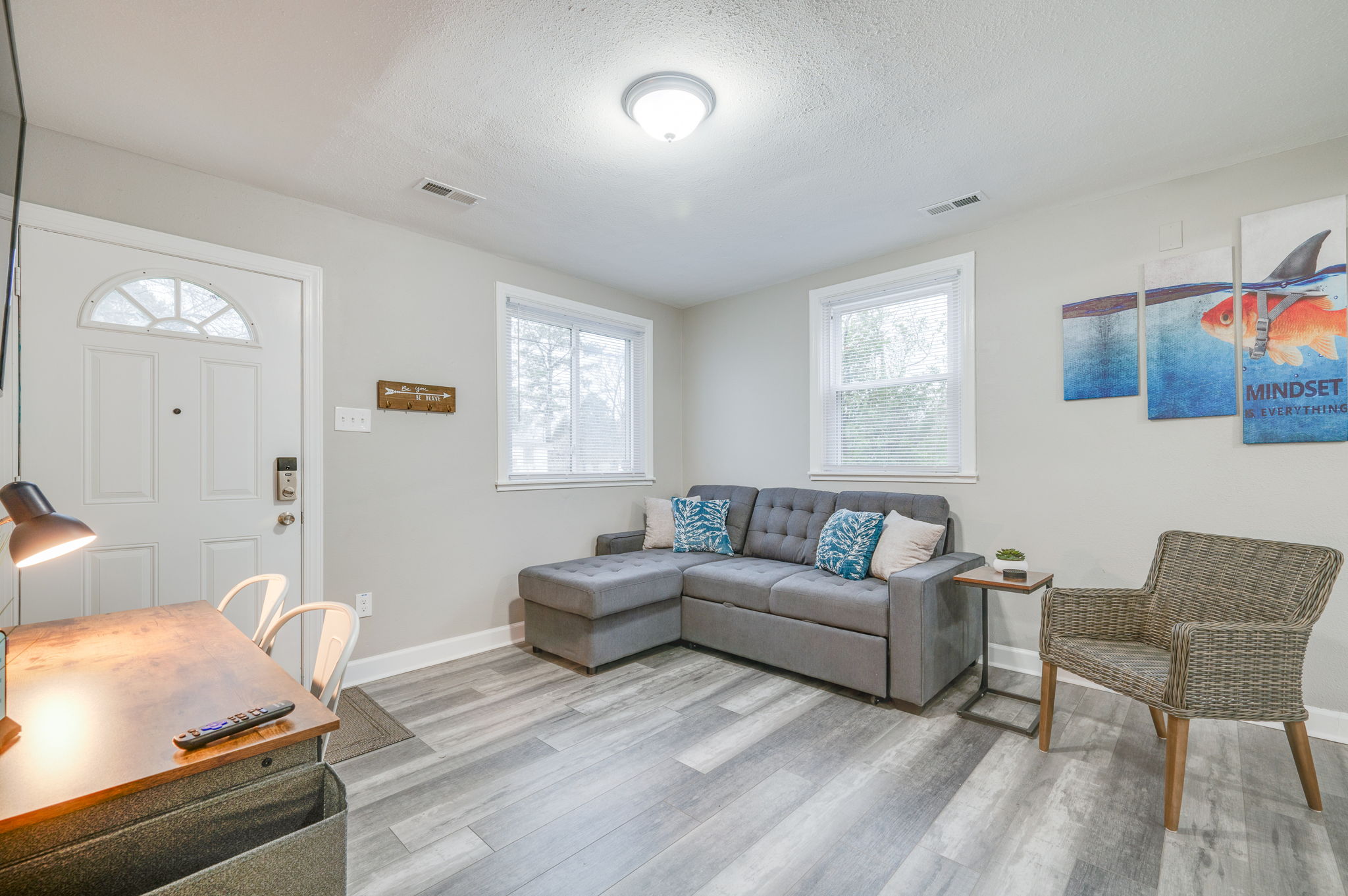 Bright living room with a gray couch, workspace, and natural light from windows.