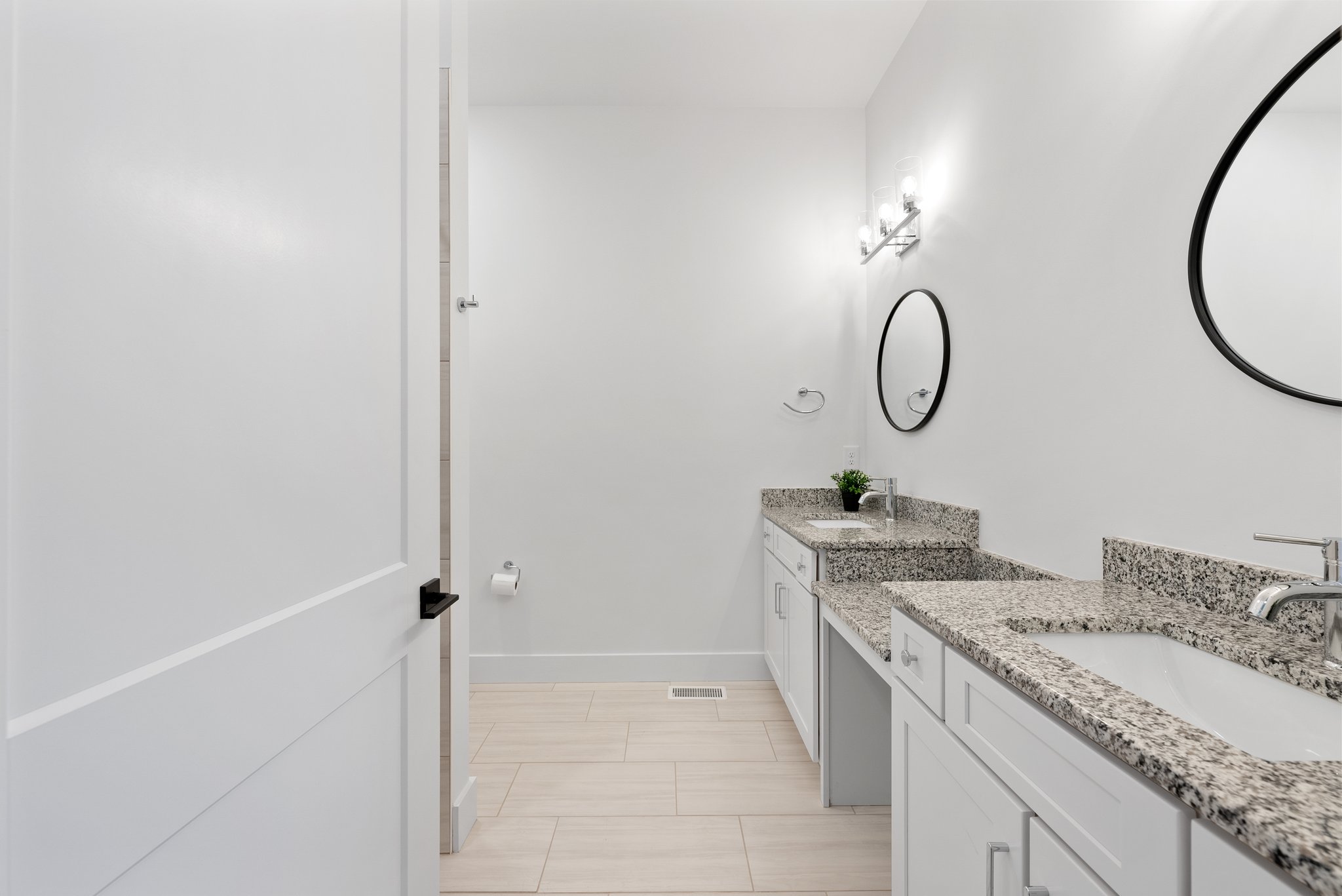 Bathroom featuring a double vanity with granite countertops, round mirrors, and modern lighting fixtures.