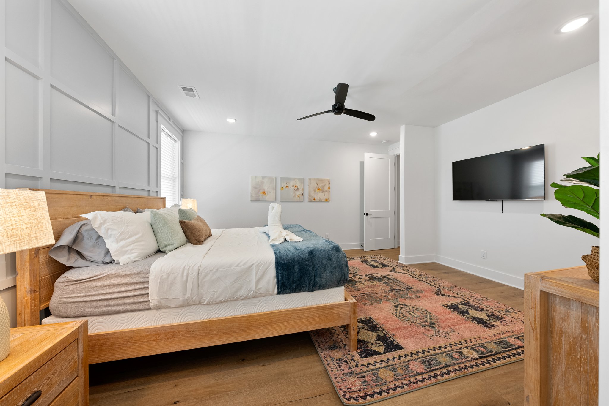 Side view of a master bedroom featuring a TV, black ceiling fan, and warm d?cor