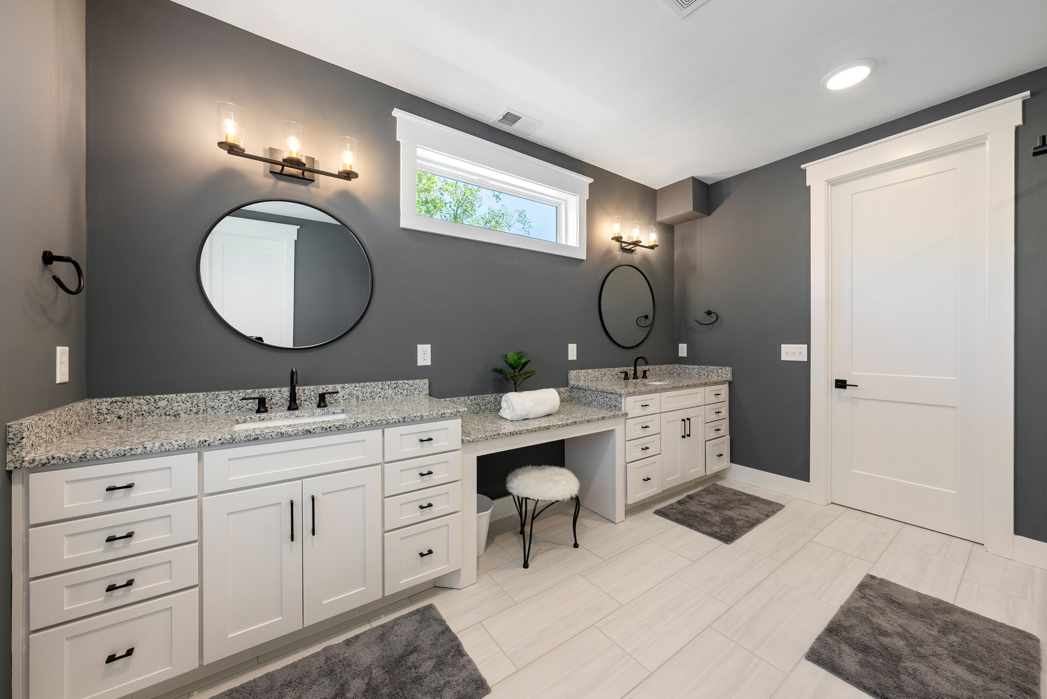 Spacious bathroom with gray walls, black mirrors, and white cabinetry