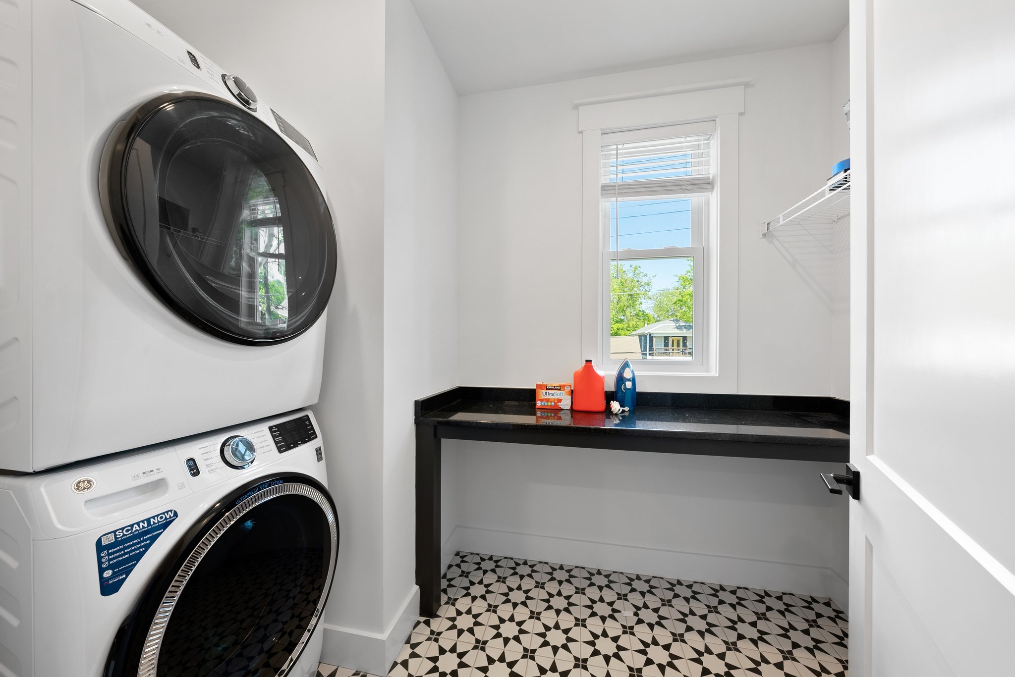A modern laundry room featuring a stacked washer and dryer, black countertop, and patterned tile flooring.