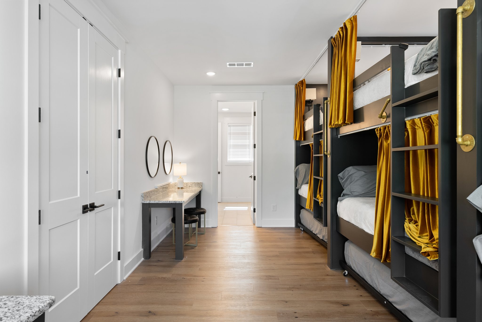 A stylish bunk bedroom with built-in black and gold bunk beds, a granite makeup tables, and dual round mirrors.