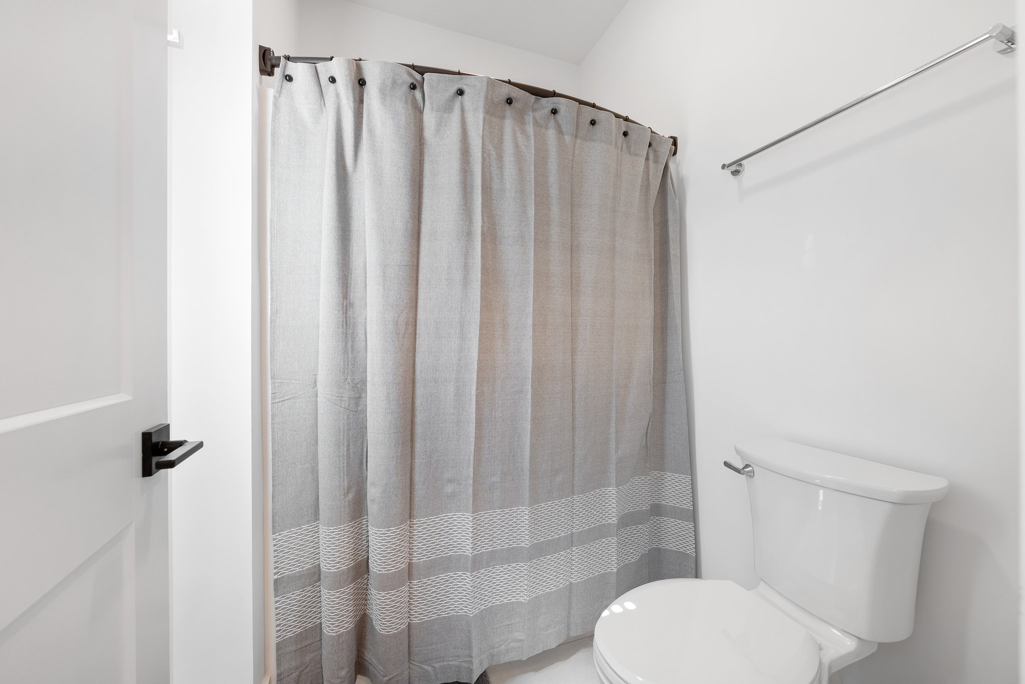 A simple bathroom setup with a toilet, white shower curtain, and towel rack.