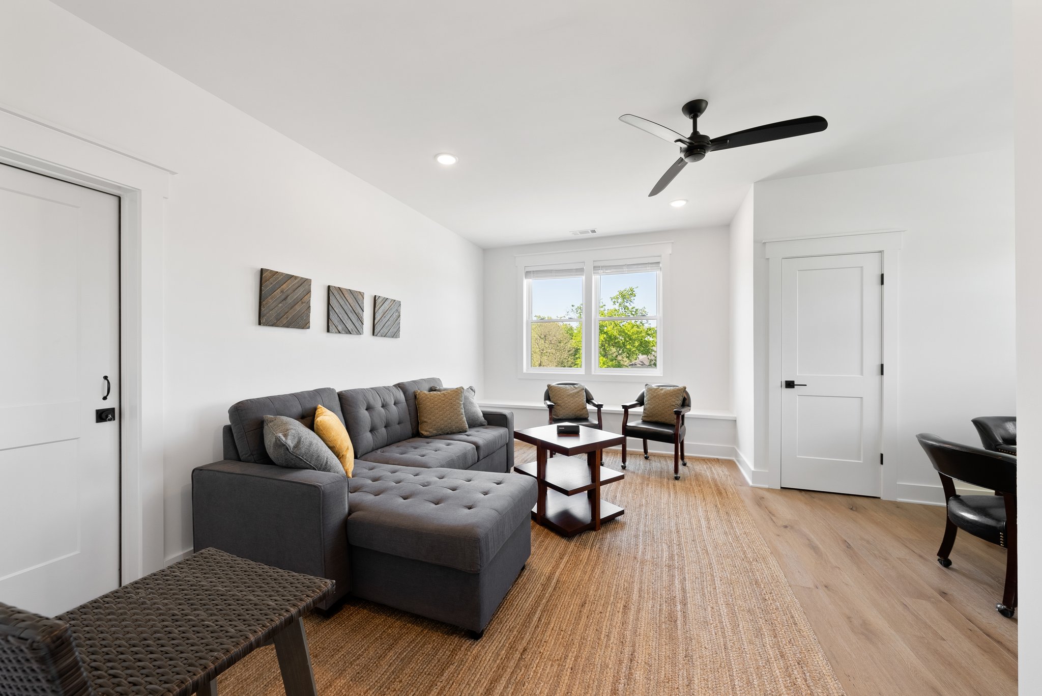 A cozy sitting area with a large gray sectional sofa, two accent chairs, and a jute rug.
