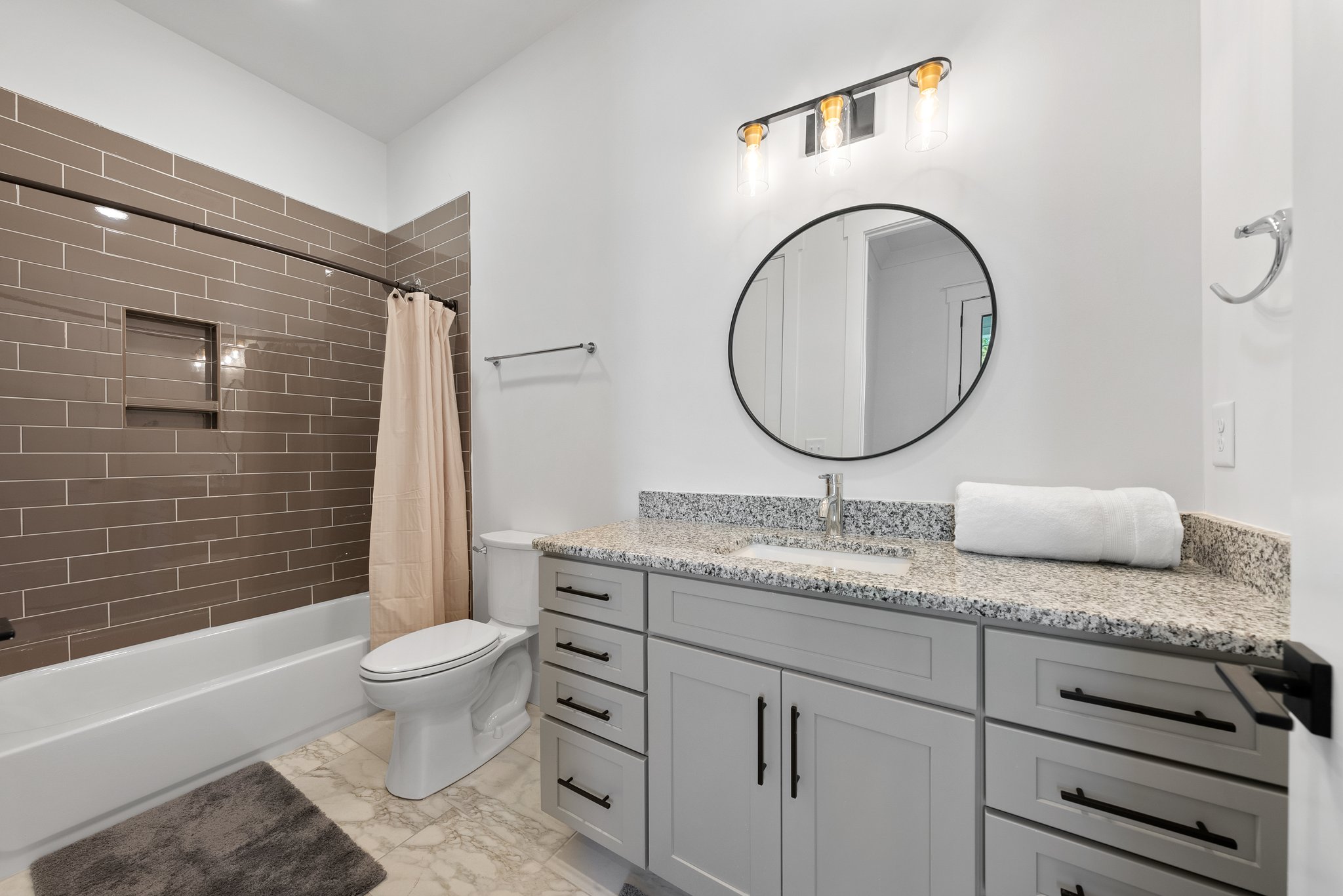Stylish bathroom featuring a granite countertop vanity, large mirror, and a tiled shower with a curtain.