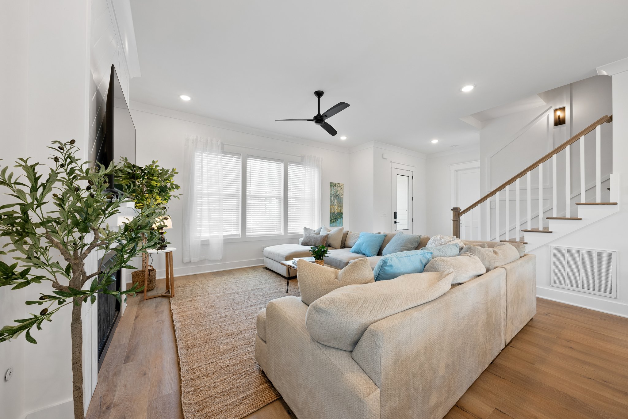 Modern open-concept living area with a neutral-toned sectional sofa, fireplace, and wooden staircase.