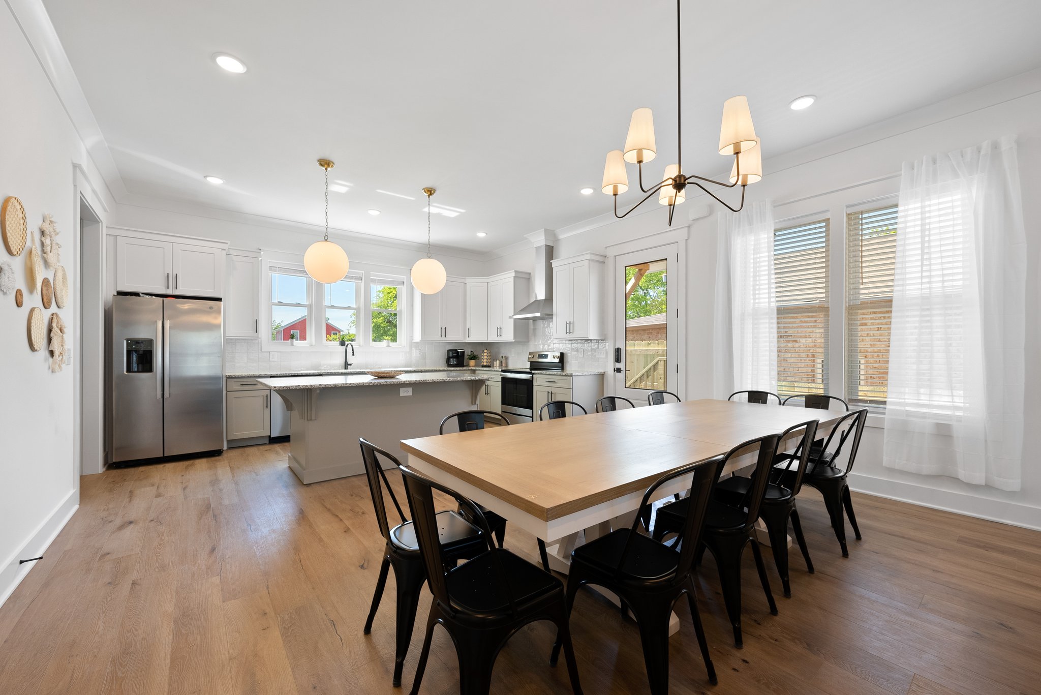 Sleek kitchen with white cabinetry, stainless steel appliances, and a large dining table with black chairs.