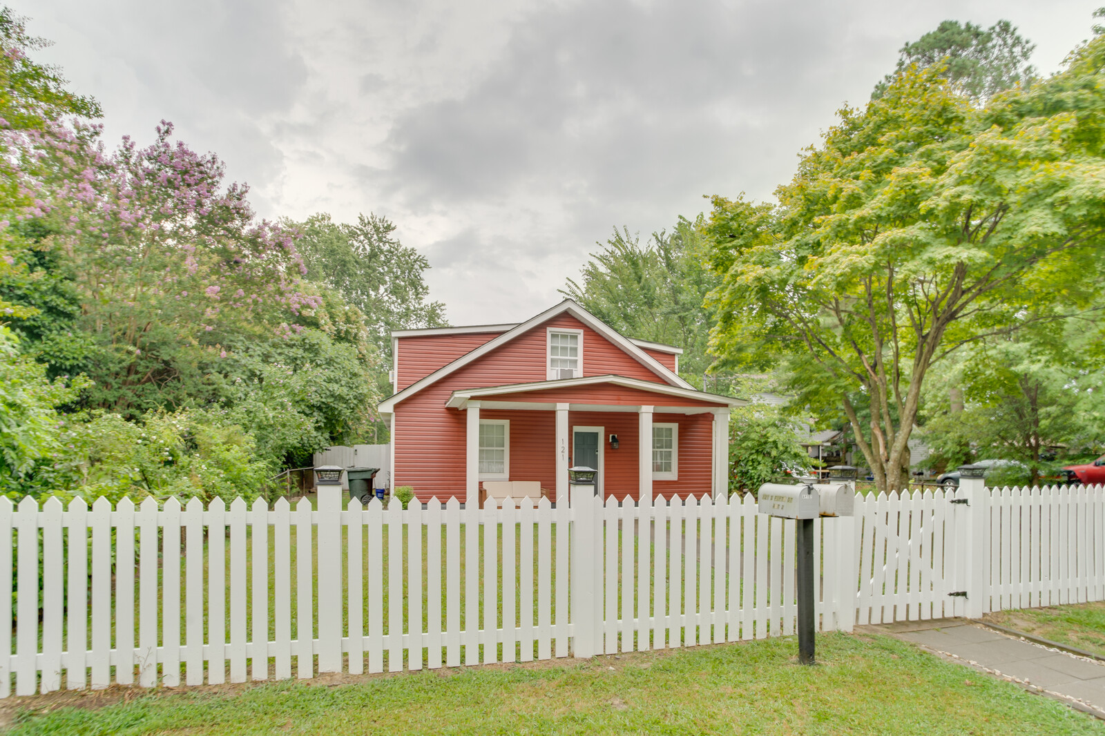 Side angle of a red cottage with a white fence and green surroundings