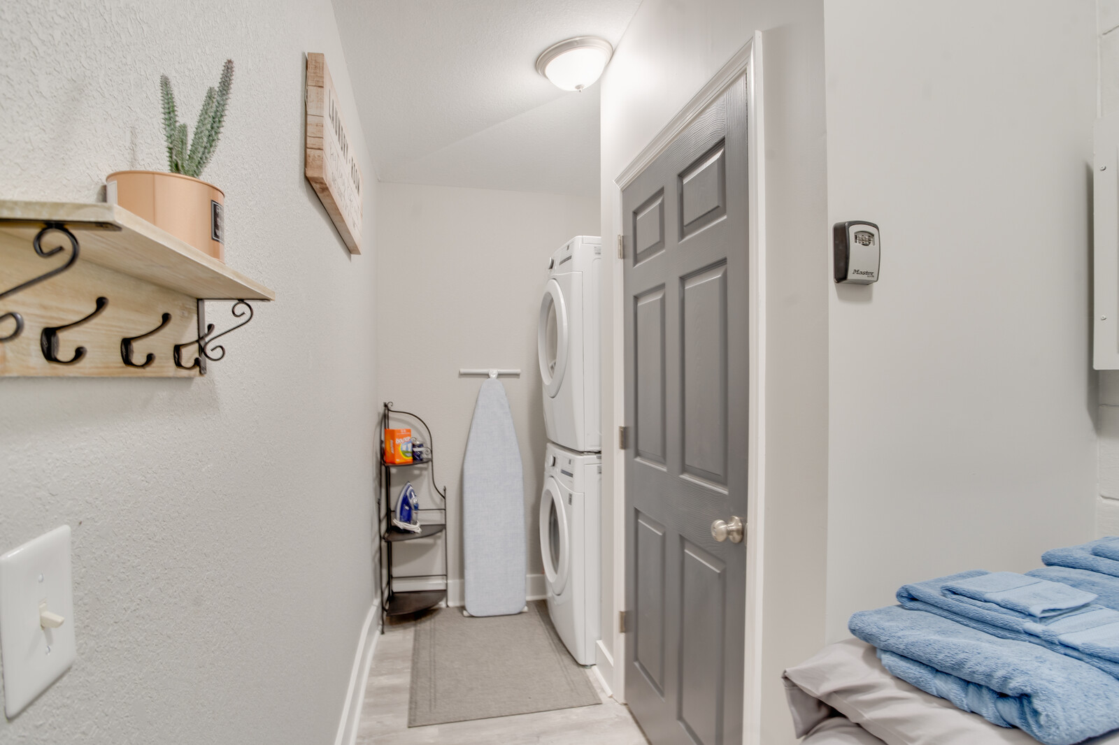 Laundry area with stacked washer and dryer, ironing board, and storage shelf