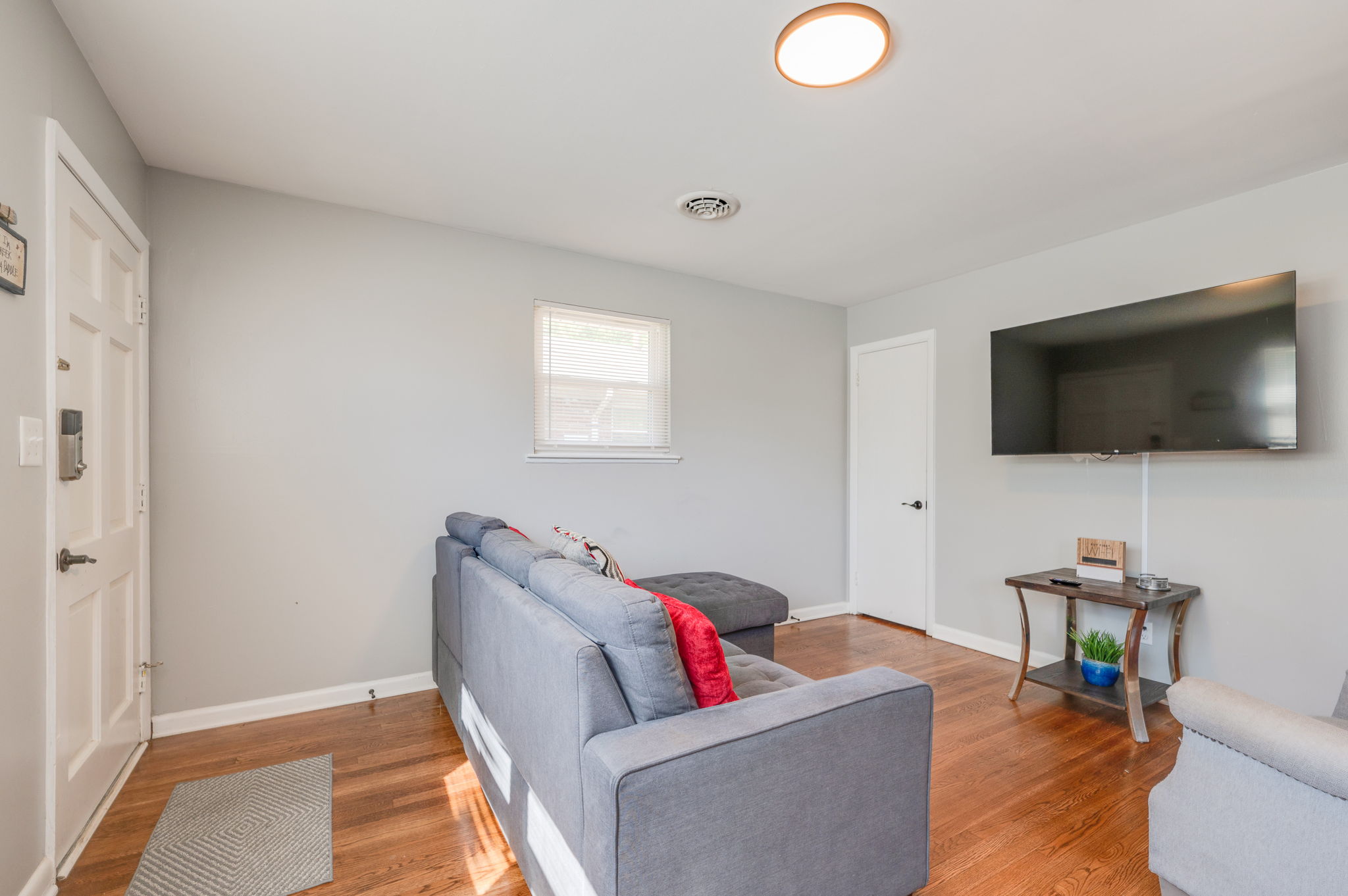 Minimalist living room with gray walls, a mounted TV, and a gray couch with red accent pillows.