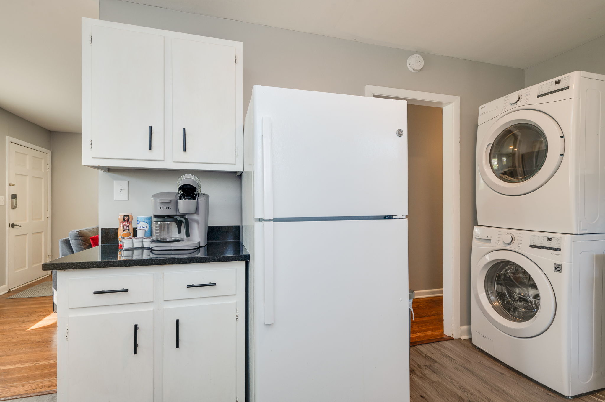 Close-up of the kitchen featuring white cabinets, black countertops, and a Keurig coffee maker.