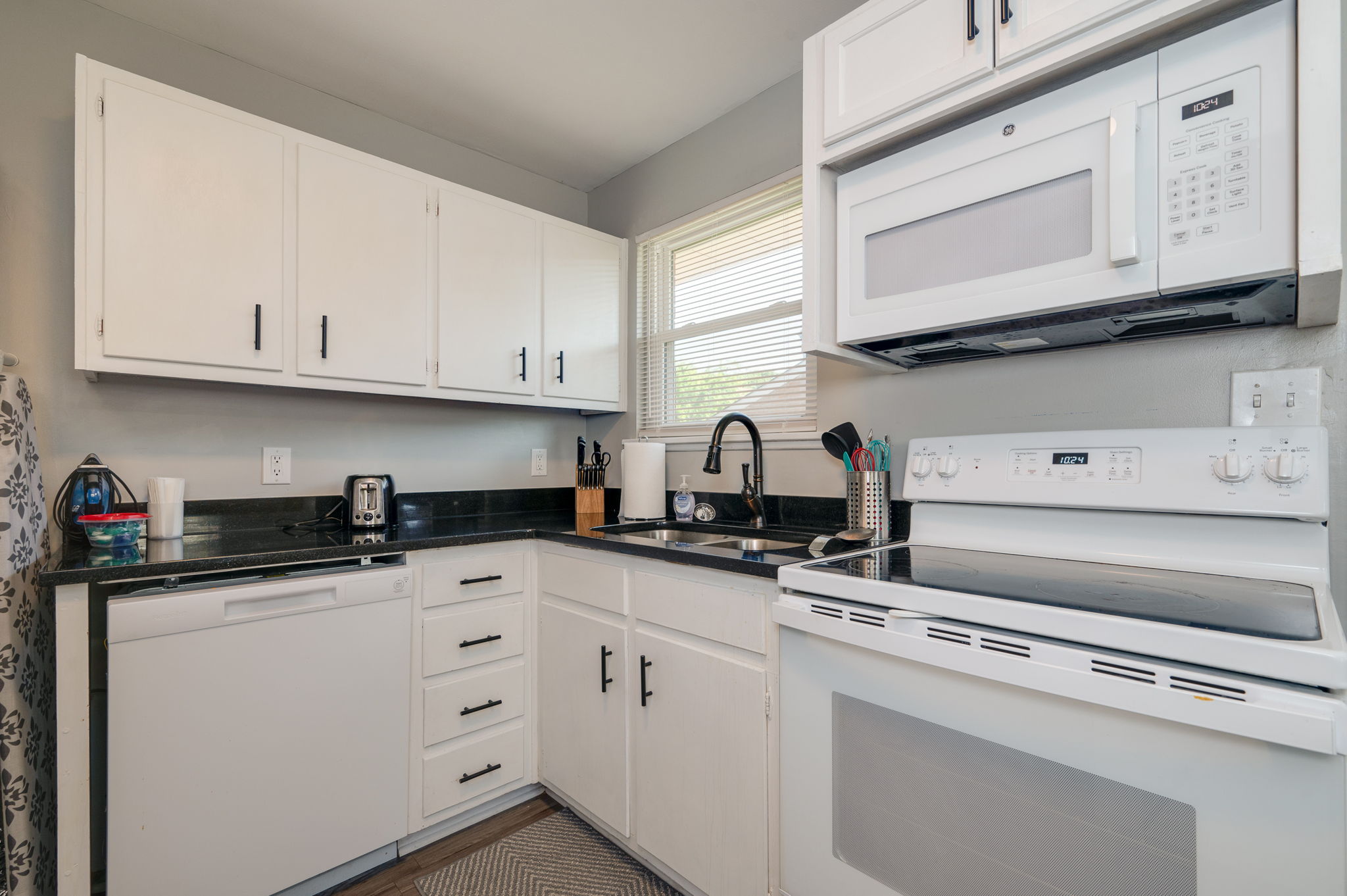 Compact kitchen with white appliances, black countertops, and a modern sink.