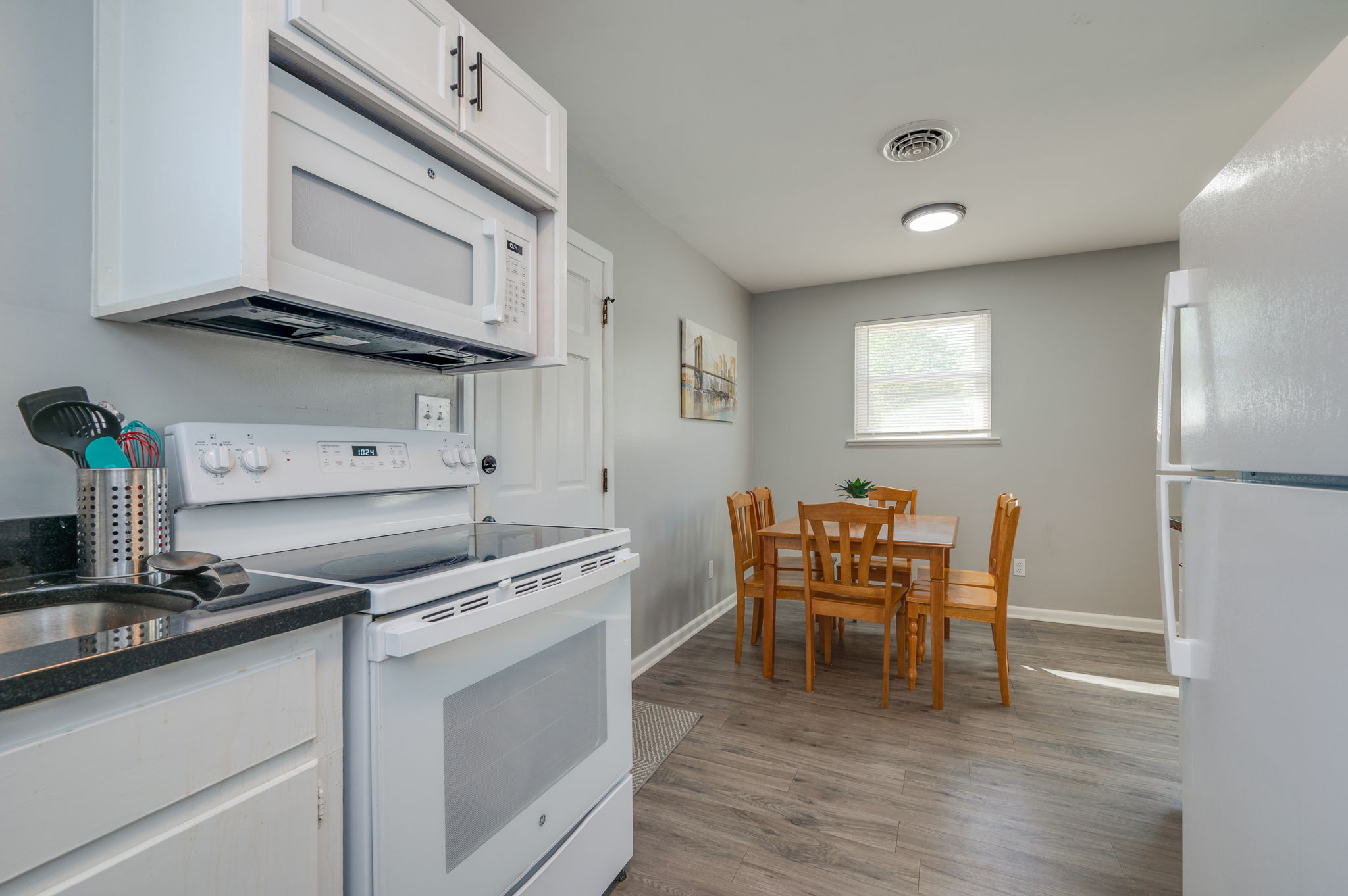 Kitchen with white appliances, black countertops, and an adjacent dining area with a wooden table.