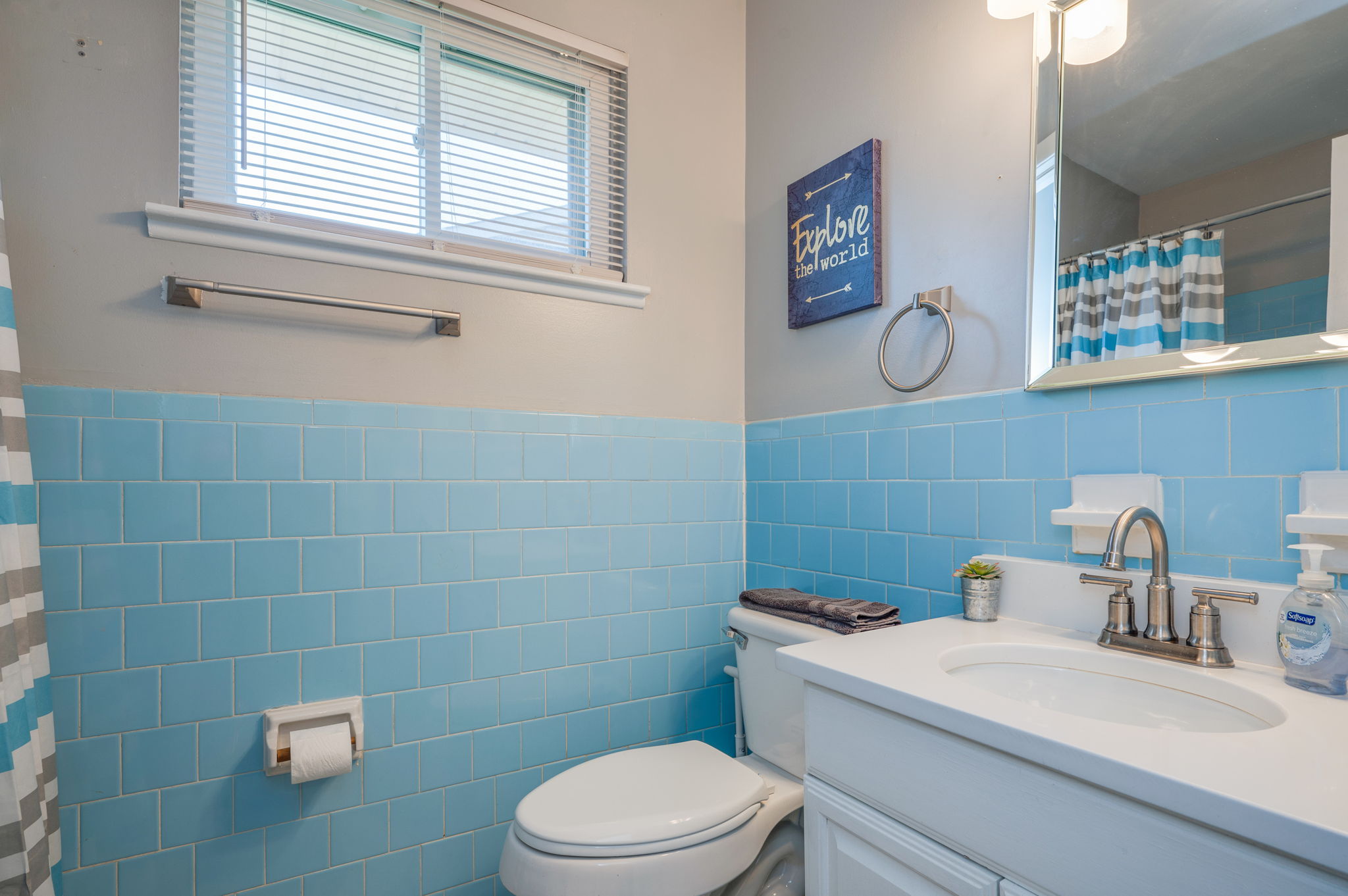 Bathroom with vintage blue tiles, white vanity, and a decorative 'Explore the World' sign.