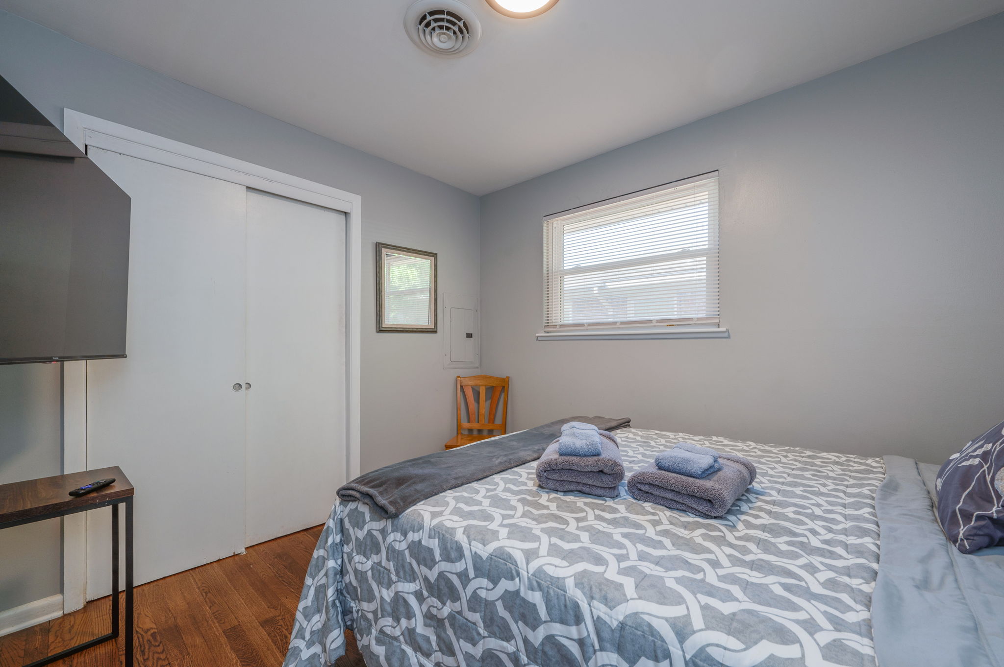 Bedroom with a neatly made bed, gray bedding, and a window allowing natural light.