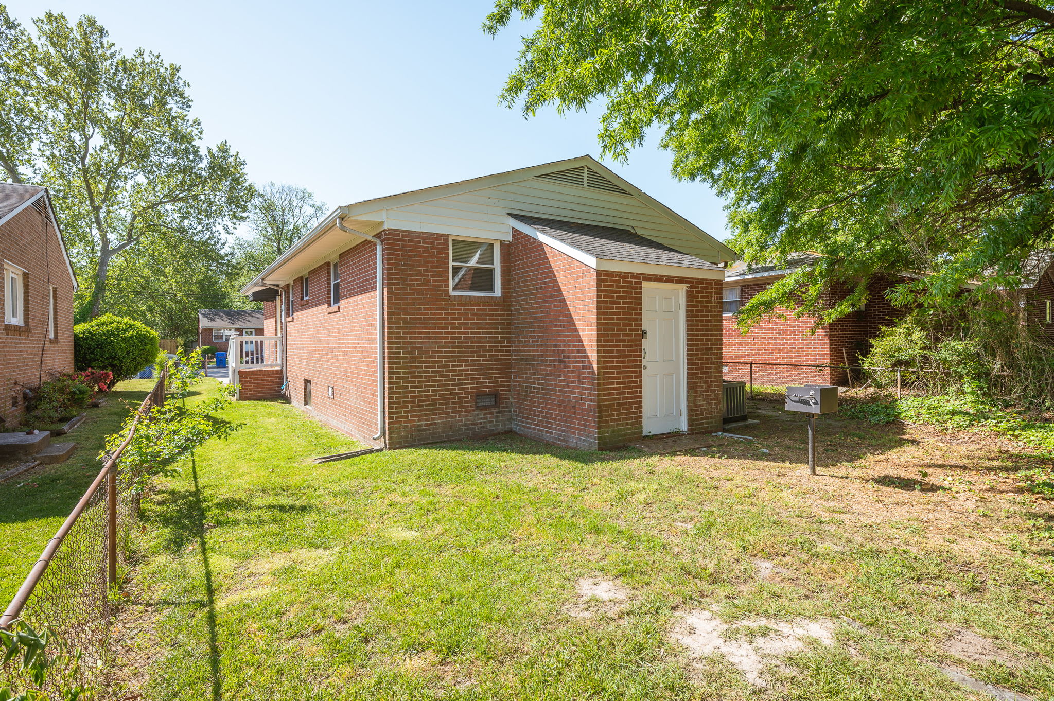 Backyard view of a brick home with a fenced-in green space and a shaded sitting area.