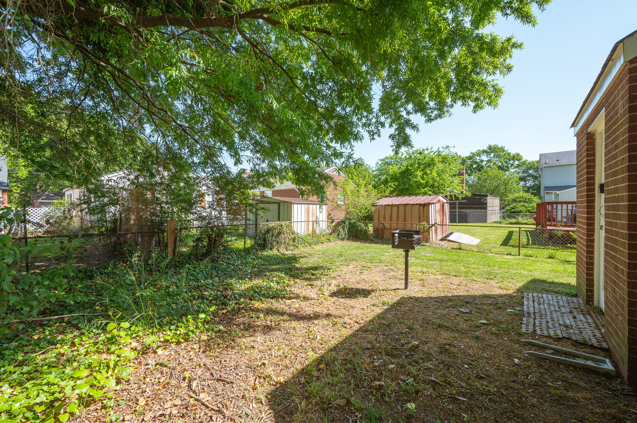 Fenced backyard with lush greenery, a shaded area, and a small barbecue grill.