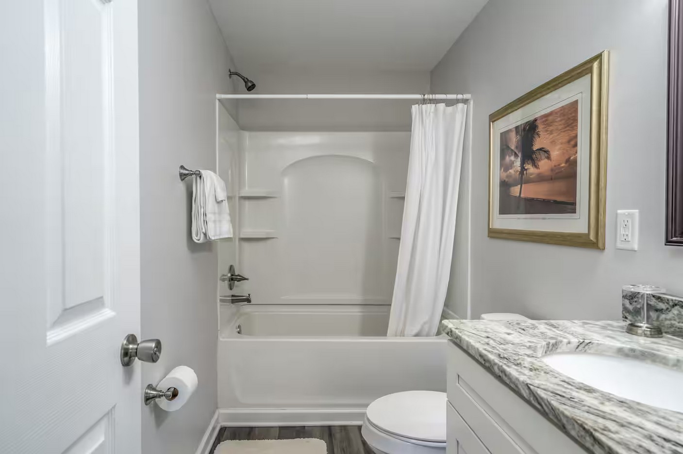 Modern bathroom with white bathtub, granite countertop, and decorative framed artwork.